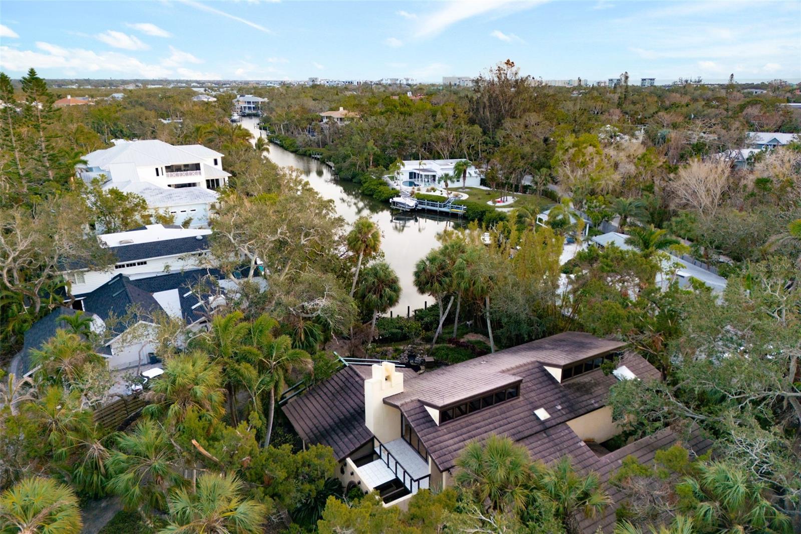 Attention architecture enthusiasts: This midcentury-modern waterfront home seamlessly blends timeless design with modern convenience. Resilient through three major storms, it sustained no damage beyond minor landscaping impacts and minimal water in the garage. Set on a lush 0.61-acre lot in the coveted Hidden Harbor neighborhood, this jungle oasis offers an unparalleled living experience. The property boasts tropical landscaping, a tranquil koi pond, and a canal-front boat dock. A circular paver driveway leads to a two-car attached garage, while the backyard oasis features a screened patio, multiple paver seating areas, and two upper-level balconies with breathtaking long canal views. Built for durability, the home includes a buried propane tank connected to a whole-house generator and an irrigation system fed by a dedicated well. Inside, the living room captivates with vaulted cypress ceilings, exposed beams, a wood-burning fireplace, hardwood flooring, and double French doors that open to the patio overlooking the canal. The dining room, adjacent to the kitchen, offers hardwood flooring, sliding glass doors, and a charming chandelier. The kitchen combines functionality and elegance, featuring granite countertops, under-cabinet lighting, and a reverse osmosis water filtration system. Upstairs, the primary suite is a private retreat with vaulted ceilings, a spacious walk-in cedar closet, and sliding glass doors opening to a balcony with sweeping canal views. The en-suite bathroom features dual sinks, a soaking tub, a walk-in shower, and vintage tile accents. An adjacent office/den offers built-in shelving, transom windows, and access to two balconies — one overlooking the canal and the other the front yard. On the main floor, the guest suite includes an 11-foot vaulted ceiling, private deck access, and an en-suite bathroom. Additional spaces include a cozy family room with dual sliding glass doors to the patio and an interior atrium filled with lush plants. Conveniently located just 1.3 miles from Siesta Key Beach and dining, 2 miles from shopping, and a short drive to downtown Sarasota, Sarasota Memorial Hospital, and the airport, this home offers both serenity and accessibility. This is a rare opportunity to own a piece of architectural history in a prime location. Experience the perfect fusion of timeless design, modern amenities, and waterfront living in this Hidden Harbor gem.