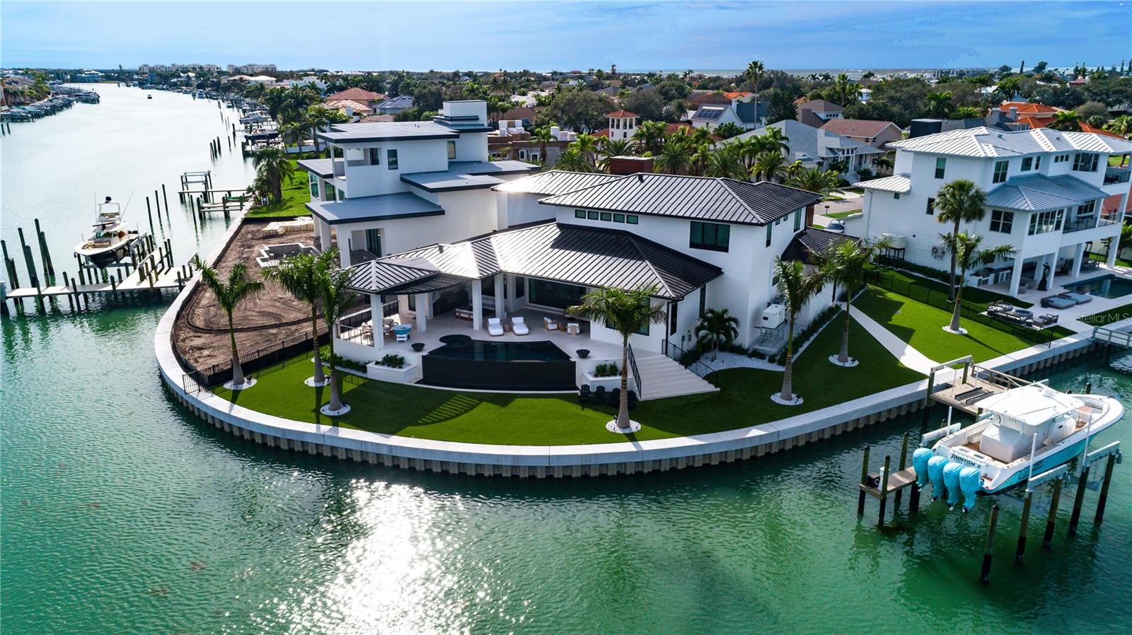 This custom luxury home, completed in 2023, exemplifies exceptional coastal living and architectural excellence, set on 200 feet of waterfront with seamless access to open Gulf waters — a true haven for boating enthusiasts. • DESIGN: Created by the award-winning Sire Design team, known from Netflix’s Designing Miami and HGTV’s Divided by Design, the home was thoughtfully designed for indoor-outdoor flow, everyday comfort, and timeless appeal. • SMARTLY BUILT: Elevated construction, impact-resistant windows, full-house generator, supported by a pilings and stem wall foundation for enhanced structural integrity. • LIVING SPACE: 5,251 square feet of air-conditioned space with 5 bedrooms, 6 full and 1 half bath, a loft, elevator, and two-2-car garages — all anchored by a dramatic 24-foot foyer with a custom pivot door. • HOME AUTOMATION: A full Savant system manages audio-visual, lighting, security, window treatments, televisions, and music — delivering seamless, effortless everyday living through a centralized platform. • INTERIOR FINISHES: Oak Plank Flooring, Avocatus quartzite, Van Gogh onyx, walnut accents, CLE tile, Atelier de Troupe lighting, and Waterworks fixtures add warmth, character, and quality throughout. • OUTDOOR LIVING: A negative-edge heated pool with spillover spa, covered lounge area, and artificial turf create a low-maintenance outdoor retreat perfect for relaxing or entertaining. • DOCK & BOATING: A custom dock completed in 2022 includes a 40,000-pound lift for a 52-foot boat, 2 JetSki lifts, and a seawall completed in 2020. There is ample space to position a larger yacht as well. • SETTING: Situated on a beautiful street in a peaceful waterfront setting, the home offers effortless access to the water, with the dock placed to the side to preserve open views. Located just minutes from beaches, parks, dining, shopping, and airports, this home offers a lifestyle defined by thoughtful design, premium finishes, and convenience — both on and off the water. Come experience the level of quality, comfort, and design that truly sets this home apart.