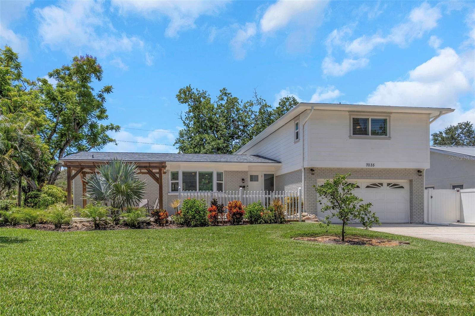 Every so often, a home comes to market that stands distinctly apart — a rare offering in one of St. Petersburg’s most treasured neighborhoods. Nestled in the historic and highly coveted Pink Streets of Pinellas Point, this split level residence masterfully marries timeless architectural charm with modern sophistication, all in desirable Flood Zone X for added peace of mind.
From the moment you arrive, the curb appeal is undeniable. Lush, green lawn, meticulously manicured landscaping, and a charming pergola create an inviting front garden retreat that offers the perfect place to relax and take in the beauty of the picturesque neighborhood.
Step inside to an airy, light-filled interior where blonde tile floors set a warm, elegant tone. The striking glass and wrought iron staircase makes a dramatic first impression, while the fully appointed kitchen exudes sleek contemporary finishes, stainless appliances, and thoughtful design details. The main level’s open layout seamlessly connects the formal living and dining spaces to a spacious bedroom and full bath, perfect for guests, a home office, or main level primary suite.
Upstairs, new hardwood floors run throughout, leading to three additional bedrooms and a full bath. The primary bedroom features a walk-in closet and an en suite bath. On the lower level, a sophisticated family room with custom built-ins and a wood-burning brick fireplace opens to a newly constructed enclosed lanai — a stunning modern take on the classic Florida room. Whether serving as a tranquil plant-filled retreat, a stylish fitness space, or a sunlit lounge for morning coffee, it invites both relaxation and inspiration.
The attached two-car garage offers ample storage, laundry accommodations, and a Tesla charging station. You’ll have peace of mind with the abundance of recent updates, including a new roof and gutters, new two-year-old HVAC, new exterior siding and paint, and impact-rated windows and doors throughout. Every renovation has been executed with precision, and no expense was spared, reflecting pride of ownership in every detail.
This is a rare chance to own a home in the Pink Streets that blends the enduring character of old Florida with the comforts of modern living. Opportunities like this seldom arise — seize it before it’s gone!