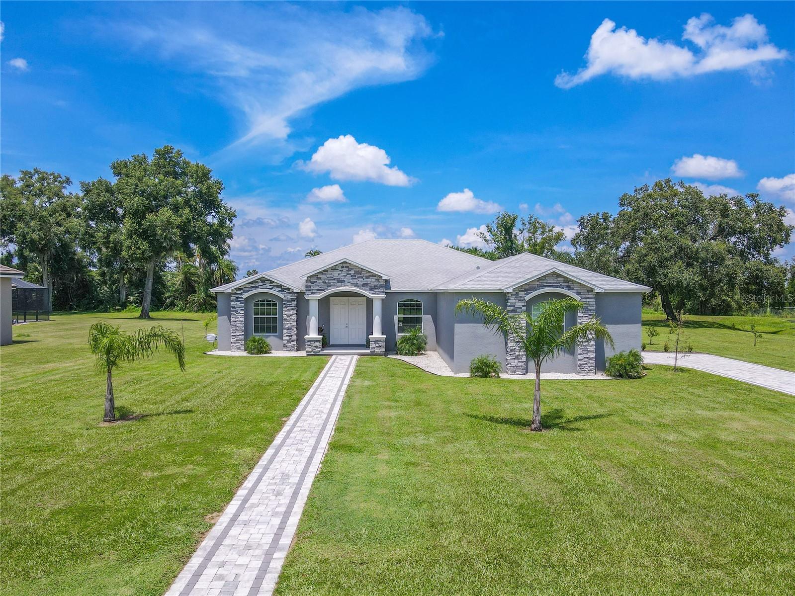 Built in 2022, this custom home is located in private 8-home community surrounded by multi-million-dollar properties. Set on an oversized 1-acre lot, the property includes deeded access to Lake Thonotosassa, the largest lake in Hillsborough County. Residents use a community easement that leads to a waterfront launch area for transporting kayaks, paddleboards, and other small craft across 839 acres of water. The location offers a serene setting with quick access to major highways, shopping, dining, and downtown Tampa. The exterior features a light gray façade with stone accents, a side-entry two-car garage measuring 25x24 feet that accommodates full-size trucks or small boats and includes overhead storage, an extended paver driveway with a matching front walkway, a double-door entry framed by arched windows, and young landscaping that enhances the first impression. Inside, an open floor plan connects the main living areas. Wide-plank luxury vinyl flooring flows through the common spaces, complemented by high ceilings and neutral finishes. Dimmable light switches throughout the home allow tailored ambiance day or night. The family room offers an electric fireplace and large windows overlooking the backyard and pool. The kitchen blends style and function with granite countertops, a center island with sink and seating for six, stainless steel appliances including an induction cooktop, a coffee and dry bar, abundant cabinetry, and two double pantries. The dining area sits between the kitchen and family room for easy everyday living and entertaining. The primary suite includes a tray ceiling, French doors to the patio, and two walk-in closets. The ensuite bath features a double granite vanity, a walk-in shower with rainfall head, and a built-in niche. A pocket door connects the suite to a carpeted fourth bedroom with Jack-and-Jill bath access, ideal for a nursery, office, or sitting room. Two additional bedrooms, each with a double-door closet, are located in a separate wing. The second full bath offers a tub and shower combination with tile surround and a granite vanity. The third bath includes a walk-in shower and granite vanity. A dedicated media room comes with an included home-theater screen and added insulation for sound control. The laundry room provides a washer and dryer, granite counters, cabinetry, a stainless steel sink, and wall hooks, plus direct access to the garage. Outdoor living centers on the screened, heated gunite pool, rectangular for comfortable lap swimming, with a paver deck, pool alarm, and views of the tree-lined backdrop. A covered patio with two ceiling fans and dual sets of French doors creates a smooth indoor-outdoor entertaining. The acre offers generous green space and fruit-producing trees. The lower rear of the property helps keep the rest high and dry though it has never flooded or held water, even in heavy rain events. Additional features include hurricane shutters for all windows, ceiling fans throughout, water filtration and softener systems, numerous extra outlets in the eaves for seasonal and holiday lighting, and a private mailbox. Appliances, all new in 2022, include the dishwasher, range, refrigerator, washer, and dryer. The property is on well water with a septic tank and drain field located on the right side of the driveway. This home pairs refined design with the rare opportunity to live near Lake Thonotosassa, offering convenience to Tampa and a luxury lifestyle.