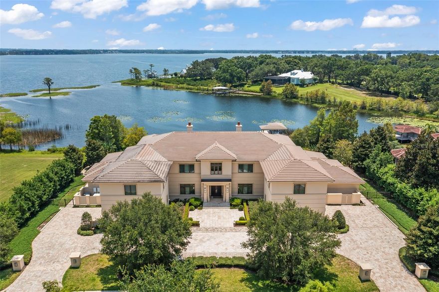 One or more photo(s) has been virtually staged. Discover the epitome of luxury living in this extraordinary custom lakefront estate, located within the prestigious gated community of Chaine du Lac. Meticulously crafted by the renowned luxury home builder, Posada Custom Homes, this stunning residence offers an unparalleled blend of elegance, privacy, and timeless appeal. Spanning over 10,000 sq.ft. of stylish living space, this 6-bedroom, 9-bath home exudes sophistication at every turn. Nestled on an expansive 1.83-acre lot, enjoy the exclusivity of approximately 200' of unobstructed lake frontage on the breathtaking Lake Butler, part of the renowned Butler Chain of Lakes. Immaculately maintained by its original owners, this home greets you with a sleek transitional elevation and meticulously landscaped grounds. As you approach, a circular driveway leads you to the grand entry, flanked by two distinct oversized two-car garages, effortlessly blending convenience and elegance. Step inside and be captivated by the seamless floor plan and impeccable finishes that create an ambiance of refined luxury. Adorned with wide plank wood flooring, the spacious great room with a gas fireplace flows effortlessly into the gourmet kitchen, overlooking the lake. Custom cabinetry, a built-in Sub-Zero refrigerator, Wolf appliances, and two generously sized islands with seating make this kitchen a chef's dream. Completing the picture is a built-in microwave, bonus cooktop and sink, and an oversized walk-in pantry. Embrace the beauty that extends beyond the interior as you admire the gorgeous views of the stunning backyard, visible from both the kitchen and the great room. The downstairs primary wing offers a private sanctuary, featuring two resort-style bathrooms, walk-in closets, and its own laundry room. Additional highlights of the first floor include a second bedroom suite, two spacious offices, and two grand floating staircases that exude architectural brilliance. Ease of access to the second floor is provided by an elevator, leading you to four additional bedroom suites, a spacious game room, library, fitness room, and two (approximately 24x30 bonus rooms) currently utilized as custom walk-in closets. This level seamlessly accommodates your lifestyle while providing the utmost comfort and versatility. Practical amenities such as two laundry rooms, seven zoned A/C units, and ample storage areas further enhance the appeal of this exceptional residence. Step outside to the backyard paradise, where a resort-style pool with a full-length sun shelf beckons you to relax and unwind. The large enclosed patio and full pool bath offer a perfect setting for entertaining, while a private covered boat dock with a lift invites you to explore the enchanting waters of Lake Butler, one of 13 pristine lakes that make up the Butler Chain of Lakes. Chaine du Lac is renowned for its generous lot sizes and is nestled within the exclusive community of Windermere. Enjoy the convenience of being just minutes away from Winter Garden Village, downtown Winter Garden, A+ schools, upscale shopping, fine dining, top area attractions, major roadways, and the Orlando International Airport.