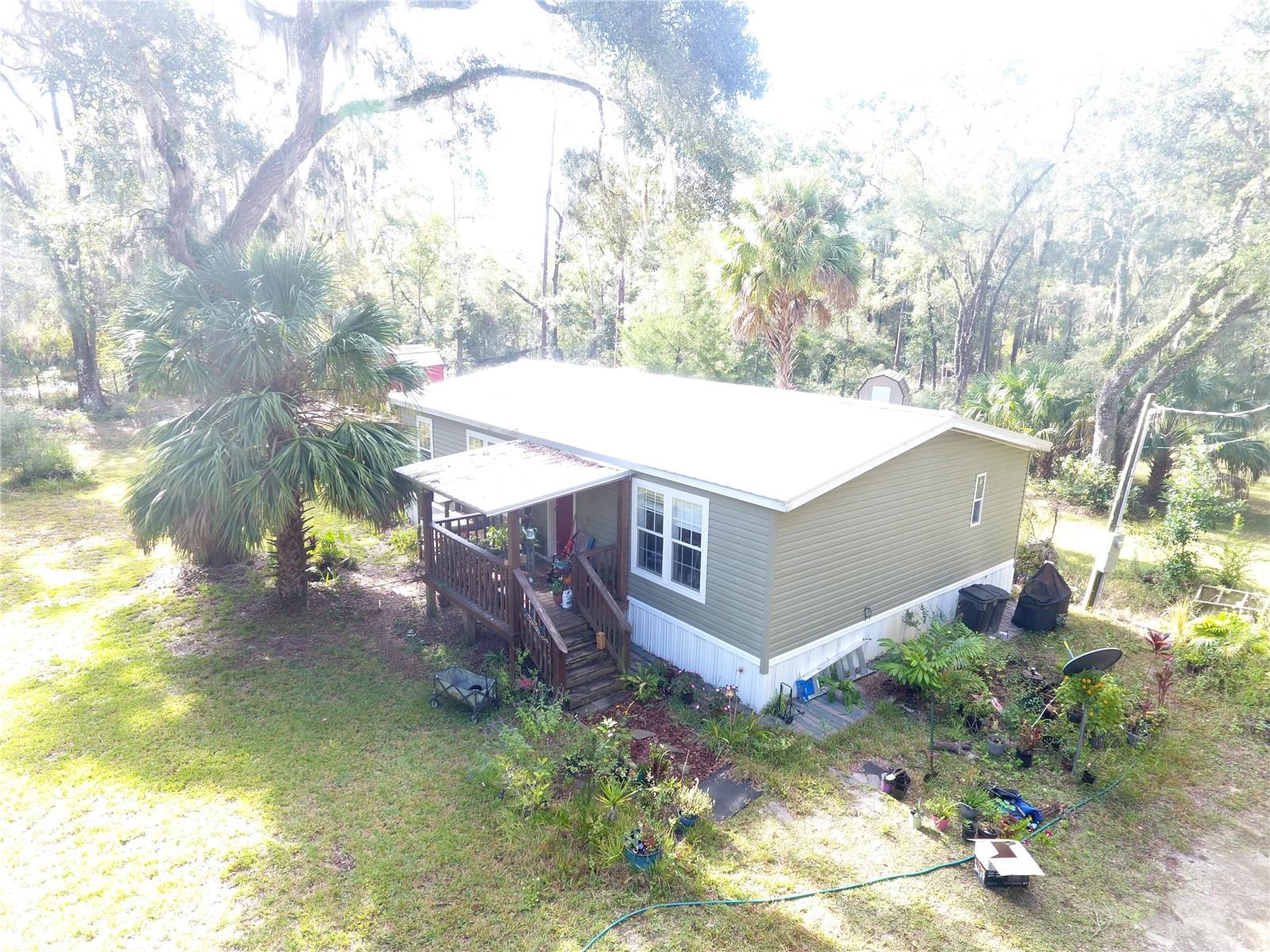 CHIEFLAND, FL ` 2014 PRACTICALLY NEW 3 bed/2 bath doublewide mobile home on 2.5 acres ~ Metal roof and A/C heat pump are only one year old! No hallways so no wasted space, just wide open floor plan, perfect for entertaining or stretching out and relaxing. Island kitchen with electric and breakfast bar, real wood cabinets, track lighting and kitchen sink window overlooks the back yard to watch the deer who frequent here. The stove is 4-burner gas with a griddle in the middle, but if you don't like cooking with gas, the electric plug is still available behind the stove. Eat-in dining area off the kitchen has chair railings and lighted chandelier. Primary bedroom is very spacious as well as primary bathroom which has a walk-in closet, garden tub, walk-in shower, and plenty of vanity counterspace. Lots of windows with blinds that are dual-pane for energy efficiency and so important for that all natural light to flow in. The walls are taped and textured, crown molding adorns the ceilings and floors. Outside there are several outbuildings which consist of a storage shed/workshop, screened room, a greenhouse, and a cute little cottage that has been finished out with flooring, walls, a loft, and a window a/c for your extra guests or make it an office if you choose. Very desirable corner lot, has two entry gates on each road providing easy access to your property for your vehicles, boats, 4-wheelers, etc. Approximately half of the property is cleared around the house with a wooded buffer along the rear perimeter for privacy and seclusion. Large beautiful grassed and landscaped front yard has fruit trees too. Welcoming covered front porch entry. Not in a subdivision, no deed restrictions, just quiet country living! Many local boat ramps, numerous pristine freshwater springs, but only 20 minutes to Super Walmart if you need to shop and 25 minutes to the island of Cedar Key and the Gulf of America. Low property taxes, and this home should qualify for all types of financing, including no money down USDA. Call for an appointment to see it today!