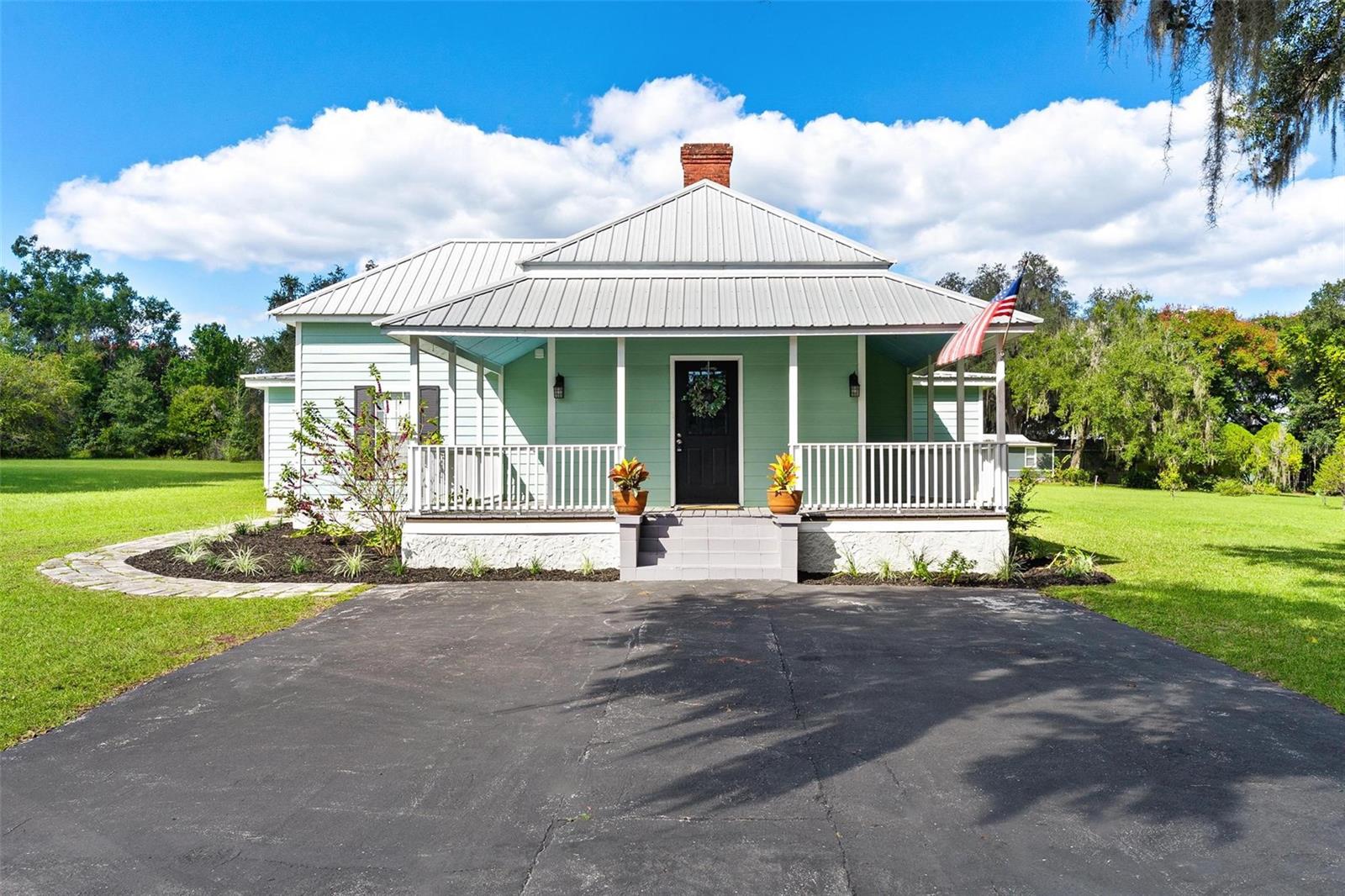 Full of charm and character, this beautifully restored historic home in Lady Lake offers the perfect blend of timeless style and modern updates. Nestled on 1.6 private acres, the property feels tucked away yet is just steps from local shops, services, and a short drive to The Villages. From the moment you arrive, the wrap-around porches and metal roof create great curb appeal. Inside, you’ll find plenty of charm with volume ceilings in both the living room and primary bedroom, accented with crown molding and decorative fireplace that adds warmth and elegance. The spacious, updated kitchen is truly the heart of the home, featuring bead board detailing, a large island with seating, an eating area, and a brand-new stove—perfect for gathering with family and friends. With 3 bedrooms, 2 bathrooms, and a convenient inside laundry room with outside access, the layout is designed for convenience! Beautiful laminate wood flooring runs through the bedrooms, while ceramic tile adds a polished finish to the rest of the home. Practical updates include a newer septic system and drain field, updated electrical service, and fresh paint inside and out. Two separate outbuildings, both with electricity, provide great storage. There is wonderful potential with the oversized parcel and a potential to divide the land and also potential to run an office or business with approval. With plenty of usable land, possibilities are endless! Come see how you can make your own history in this special Lady Lake treasure!