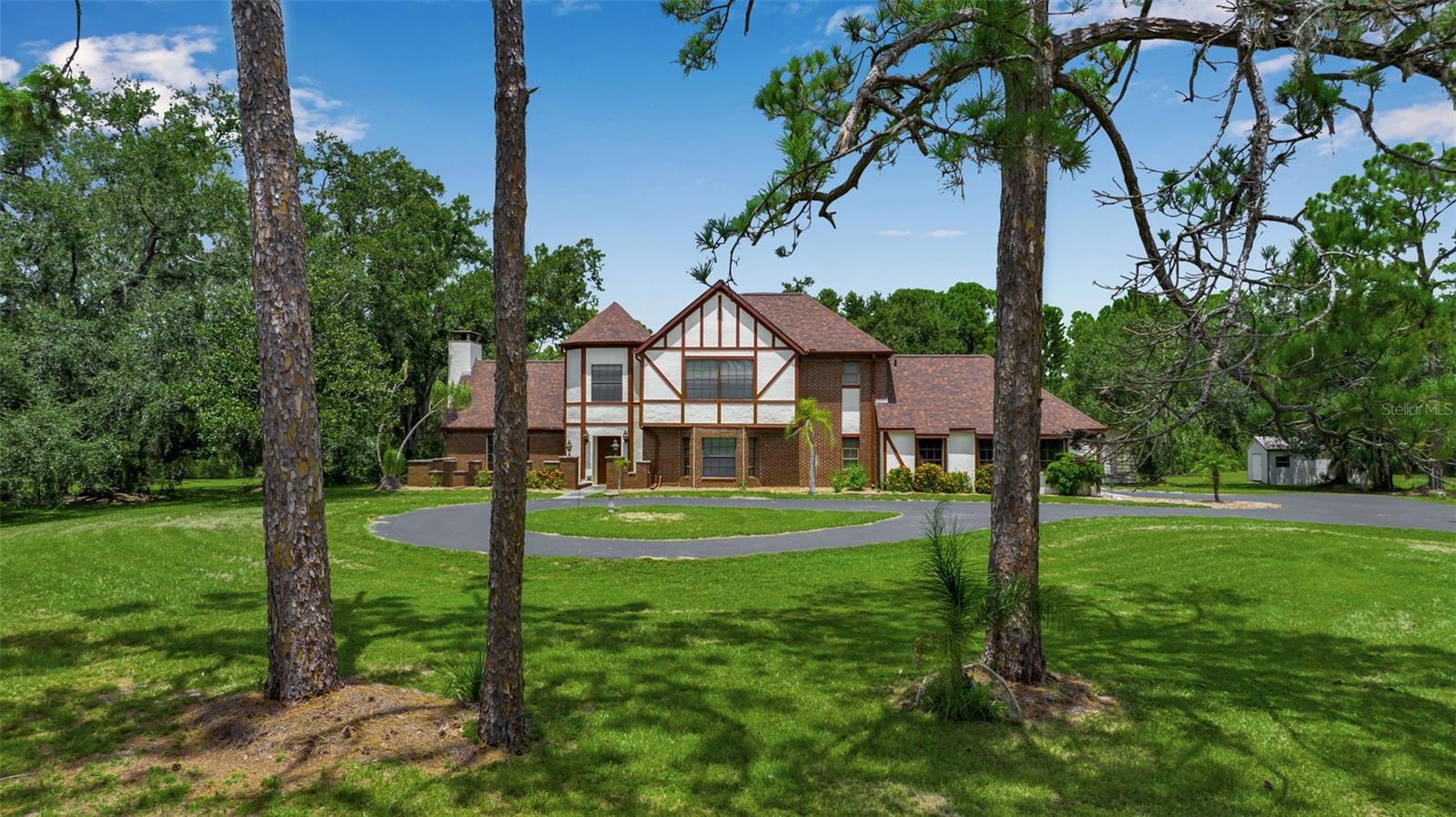 A remarkable English Tudor-designed home located in the beautiful Gator Creek neighborhood. Situated on nearly 6 acres in a private cul-de-sac, this property offers a serene country setting with majestic oaks and pines. The home features gleaming wood floors, an updated kitchen, and a living room with soaring beamed ceilings and a wood-burning brick fireplace. The kitchen and family room create a comfortable gathering space, complete with a dry bar that can be converted into a wet bar. You'll also find a separate dining room overlooking the large lanai and pool, and a spacious downstairs office with similar views. Upstairs, the main bedroom is filled with natural light and includes newer carpeting, two walk-in closets, and an updated bathroom with dual sinks, a tub, and a walk-in shower. There are also two guest bedrooms; one is carpeted, and the other, currently used as a sewing/quilting room, has vinyl planking. The owners have diligently maintained and improved the property. Notable updates include a 20 x 30 shed installed in 2020, a new pool cage and roof in 2023, newer appliances, and a repaved driveway in 2018. The home also has two-zone AC units, with the downstairs unit installed in 2017 and the upstairs in 2020. The lot includes a pond that can be made visible from the house. This property is not in a flood zone and has experienced no water intrusion from past storms. With a little tender loving care, this home is ready to shine. Several schools nearby such as The Classical Academy, New Gate Montessori School, Prew Academy, Sarasota Suncoast Academy, Pine View School for gifted students, and Riverview High School. Siesta Key Beach is 30 minutes away, UTC mall 10 minutes, downtown Sarasota 20 minutes. Privacy, and convenience...priceless! Schedule your personal showing today.