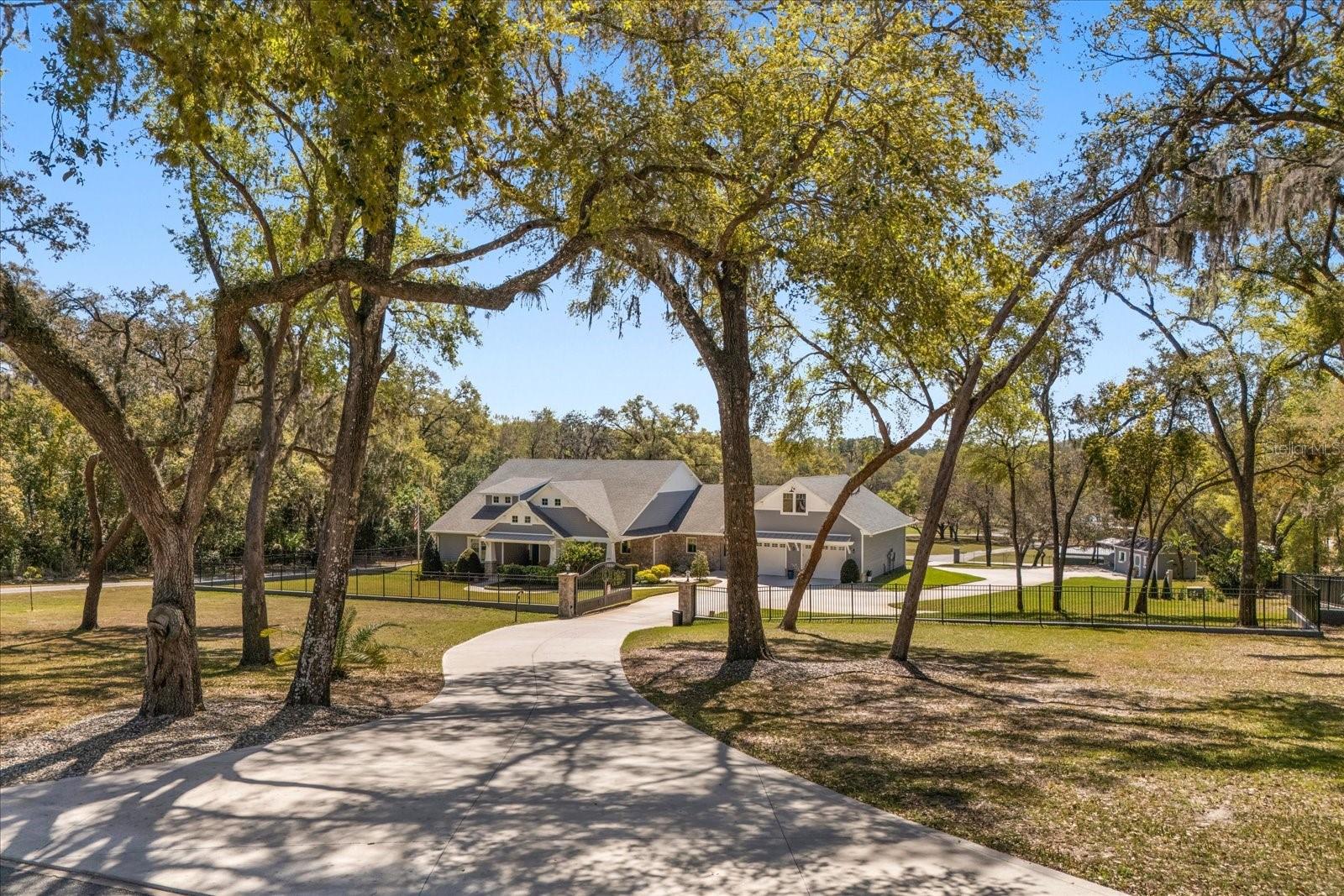 This 7-plus acre estate blends country charm and modern conveniences with scenic rolling lawns, mature trees, a private pond and multiple buildings. The stunning custom-built home features a spacious front porch where one could spend hours enjoying the beauty of the outdoors. Inside, you’ll find gorgeous hardwood floors and plantation shutters throughout the home. Soaring beamed ceilings crafted from 100-year-old barn wood creates a warm ambiance. The kitchen stands out with custom 52” cabinetry, a copper farmhouse sink, natural stone chiseled-edge counters, and a 9’ reclaimed wood island with swiveling barstools. The primary suite doubles as a safe room with a concrete roof hidden beneath a decorative tray ceiling. Its en-suite bath includes split vanities, a walk-in closet, a double shower, and a claw-foot tub illuminated by a vintage 1930s light fixture. In addition to the three bedrooms, the home also includes a dedicated office with a private entrance, and an expansive screened back porch which invites you to sit and enjoy scenic views of your private ranch. Impact-resistant casement windows, Therma-Tru exterior doors with a multi-point locking system, a hard-wired Ring security system, and fully fenced grounds—including 2 acres enclosed with aluminum fencing on a 2’ concrete wall with custom steel gates—ensure peace of mind. An impressive 1,835 SQFT attached drive-through garage accommodates 4+ large vehicles and includes a workshop, ample storage shelving, and attic access via a Versa Lift attic system. Included with other buildings situated toward the middle of the property is a 12’x24’ pump house, which houses the irrigation well pump and the standby 20,000 watt whole-house diesel generator and offers cover for the 500-gallon diesel tank. Additionally, you’ll find a 15’x24’ air-conditioned cottage perfect for multiple uses, and two Pole Barns (22’x34’ and 60’x32’) with concrete floors and a 50-amp RV hook-up. Located just 2.5 miles from Mount Dora's vibrant historic district, this exceptional ranchette blends modern comforts with serene country living. Come experience this remarkable property in person and see its exceptional features firsthand.