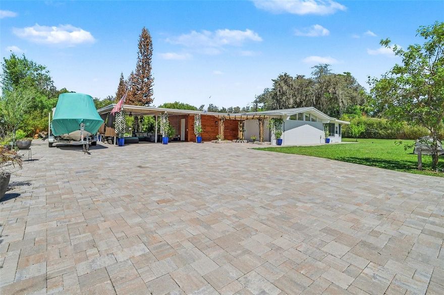 Step through a striking solar-powered iron entry gate and into a one-of-a-kind mid-century modern retreat that effortlessly blends style, comfort, and functionality. Situated on a spacious 0.57-acre corner lot, this property immediately impresses with its beautifully pavered parking and entertaining area, leading to a warm, stained wood accent entry framed by trellises draped in blooming wisteria—an inviting introduction to the home’s seamless indoor-outdoor lifestyle. Inside, nearly 2,000 square feet of thoughtfully updated living space awaits. This 3-bedroom, 2-bath home is filled with contemporary touches, including three eye-catching shiplap electric fireplaces, soaring vaulted ceilings, and high accent windows that flood the living room with natural light. Stylish barn doors, luxury vinyl and tile flooring throughout, and a designer kitchen featuring a glass backsplash, farmhouse sink, and butler’s pantry elevate both form and function. The Florida room is a true highlight, complete with two sets of hurricane-impact French doors that open effortlessly to the expansive backyard—perfect for entertaining or relaxing year-round. The guest bathroom boasts a spacious walk-in shower with a lifetime warranty, adding both luxury and peace of mind. Outside, the property continues to impress. Privacy is enhanced by lush clumping bamboo lining the perimeter, while a 900 sq ft patio offers ample space for gatherings under the open sky. There’s dedicated RV parking with a 50-amp hookup, plus a versatile 264 sq ft shed equipped with 30, 110, and 220 electrical service. Additional upgrades provide long-term value and convenience: full repipe (2018), new roof (2021), A/C replacement (2023), and an updated electrical panel (2024). A whole-house propane generator ensures you’re always prepared. Nature lovers will appreciate the abundance of fruit trees—Barbados cherry, pear, peach, lemon, fig, and key lime—creating your own private oasis. The home is currently on well water, with the option to connect to city water if desired. This is more than a home—it’s a lifestyle. Don’t miss your chance to own this beautifully upgraded, move-in-ready gem designed for modern living and unforgettable entertaining.