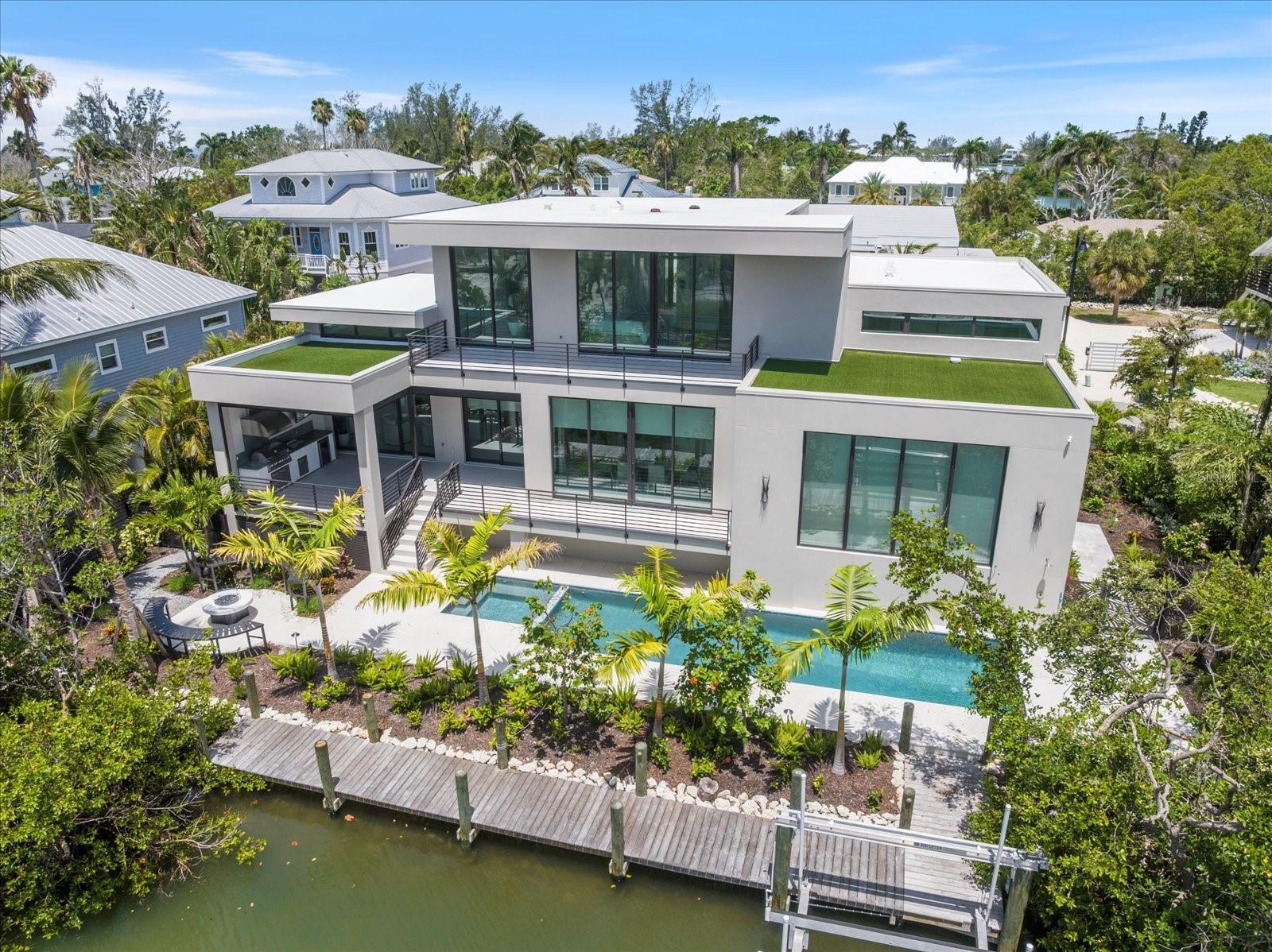 Step into a new era of coastal modern living with this breathtaking, newly constructed waterfront retreat, perfectly positioned on the exclusive north end of Longboat Key. Designed with intention and offered fully turnkey-furnished, this residence is a refined sanctuary where architectural elegance meets cutting-edge technology and relaxed sophistication.
The grand entry leads into a dramatic great room, showcasing driftwood-accented ceilings and expansive floor-to-ceiling windows that flood the space with natural light. From here, the home flows effortlessly into the open dining area and chef’s kitchen, where rich wood-tone custom cabinetry, premium appliances, and clean modern lines create an atmosphere of understated luxury.
Just off the dining space, you’ll find an expansive entertainer’s room with its own full bath—ideal for hosting dinner parties, events, or enjoying a night in with guests. Upstairs, the home’s private quarters await. Bedrooms two and three are located on the second level, while the third floor is reserved entirely for the primary suite, accessible by private elevator.
This executive-level retreat features multiple walk-in closets, serene private balconies overlooking the water, and a spa-inspired primary bathroom designed with curated finishes and timeless style.
Throughout the home, attention to detail is evident in every finish and feature—including a full Lutron lighting system, motorized shades, integrated surround sound, and a Brinks security system with CCTV monitoring.
Outside, the coastal lifestyle truly comes to life. Enjoy a resort-style pool, fire pit lounge, and a brand-new private dock just a few homes away from open water—offering easy access to the Gulf and endless boating adventures. This property was crafted to bring people together, whether relaxing with family or entertaining in style.