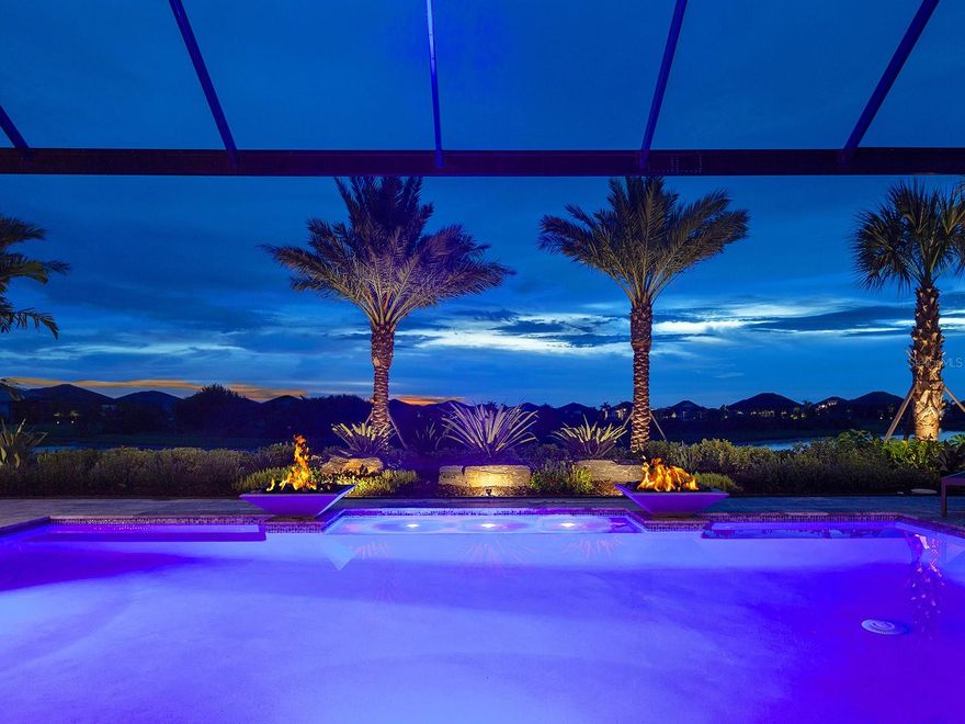 Welcome to one of the most elegant and luxurious residences in all of the Lake Club. This 2021 Margo III home highlights the best of construction and design with numerous luxurious upgrades. Designed by Boutique Interiors, every inch of this residence has been carefully selected to evoke an opulent lifestyle set amidst over 100 feet of lakefront and preserve views. Elevating this home to the highest level, the current owners have meticulously upgraded the interior and the grounds throughout 2023-2024 for a truly one-of-a-kind luxury property hard to replicate anywhere else. Nestled among over 800 new plantings and trees and 150 new landscape lights, the exterior showcases elegance. Enter through the double glass and iron impact front door to a voluminous foyer where you will see the magnificent finishes of this home including porcelain tile flooring, custom ceilings, custom window treatments, high-end chandeliers, light fixtures, and designer finishes. The great room showcases a feature wall of designer textured paint, custom designed niches and display shelves, and lighting to display artwork or function as an entertainment center. Through 10’ impact sliding glass doors that pocket completely into the wall, the vistas of the sparkling lake and lush preserve provide the perfect backdrop. The chef’s kitchen has the culinarian in mind offering a 2021 stainless KitchenAid appliance suite, quartz counters, large walk-in pantry with completely custom shelving, and upgraded cabinetry. The adjacent dinette is a casual space for weeknight meals, while the formal dining room with its crystal chandelier centerpiece sets the stage for unforgettable dinner parties and holiday meals. The epitome of a luxurious Florida lifestyle is found on the spacious paver lanai complete with an entertaining area with a cozy fireplace and motorized sunshades, dining area, gourmet outdoor kitchen, and additional patio space. Soak in the sparkling heated saltwater pool with its fire bowl features, large sunbathing shelf, and sunken spa while enjoying the verdant landscaping and lake views through panoramic screen enclosure. The comforting primary suite is enhanced by the custom ceiling and bright French doors, plus California Closet built-ins in your dual walk-in closets, and a custom morning bar. Relax in the primary bathroom surrounded by designer wallpaper and warm neutral tones while soaking in the modern freestanding tub or savoring the spacious walk-in shower. Guests will enjoy their own elegant accommodations, in two bedrooms each with private en-suite bathrooms, walk-in closets, space for a king bed, and fine upgrades. The spacious bonus room showcases another dry bar with designer finishes and entertaining space. There’s even a pocketing door to create a private in-law suite wing encompassing a bedroom, two bathrooms, and the bonus room with lanai access.  Complementing this spectacular home is a stately study, functional laundry room, and oversized 3-car garage with its own insulation and AC splitter. Peace of mind is secured with full impact glass throughout;  2023 Generac 27kw whole-house generator with liquid cool; 2023 Culligan water softener, filtration, and reverse osmosis system; 2023 Lutron lighting system; 2023 smart systems; solid-core doors; and more. The Lake Club is a premier, gated community including a Grande Clubhouse, restaurant, pool, tennis, pickleball, playground, basketball, Linear Park, fitness center, dog park and interlinking lakes.