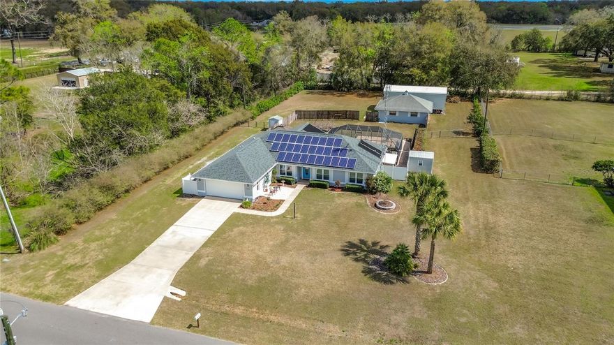 On this beautiful one-acre NO HOA property, in addition to the well-designed custom-built pool home, are Three Outbuildings!!!  (1) Full size two car enclosed garage built with concrete blocks and well insulated, currently used as a workshop; (1) Tall RV carport; (1) small carport.  On the property is a backup 20 KW commercial grade diesel generator fueled by a 200-gallon tank and a smaller 30-gallon tank. There is a chain link fence fully enclosing the backyard.  The home was just painted this year.  The home features a split floor plan, large eat in kitchen with pantry, whole house water softener system, built in vacuum system, the primary bedroom is ensuite with a large walk-in closet with 36” doorways; and all new windows in 2024!  The caged Salt and Solar heated pool have newer systems in place.  When not playing in the pool, you will appreciate the inviting Florida room for relaxing and enjoying the view of the flowering trellis and Gazebo.  And no worries about the electric bill as there are 30 fully paid and transferable Voltaic Solar panels installed on the roof, which was replaced 12/2021, all with existing warranties.  New attic insulation was installed in early 2025, further enhancing energy efficiency.  Over the years, the original and only owners have gone above and beyond to maintain this property.  It is truly to be appreciated as your next investment!