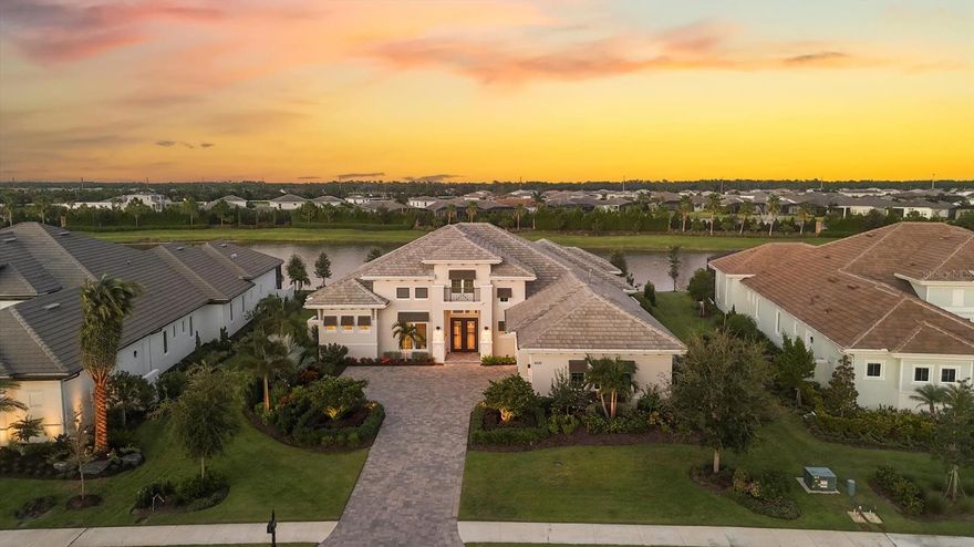 Welcome to the stunning Gardenia II model by Stock Signature Homes—where luxury meets livability in this impeccably designed four-bedroom, 4.5-bath residence. On a prime lot with expansive water views and no rear neighbors, this home is a private tropical retreat from the moment you arrive. A paver driveway and lush, manicured landscaping set the tone for what awaits inside. Go through elegant glass double doors into a bright, open-concept floorplan filled with natural light. Soaring ceilings, crown molding, neutral white oak engineered hardwood flooring and designer finishes—including plantation shutters and tasteful draperies—create a warm and elevated atmosphere throughout. The spacious great room features a coffered ceiling, built-in shelving and sleek floating shelves, ideal for entertaining or relaxing in style. The gourmet kitchen is a chef’s dream, with quartz countertops, soft-close white cabinetry, under-cabinet lighting, a large island with abundant storage, walk-in pantry and JennAir stainless steel appliances. The formal dining room just off the kitchen includes a dry bar with wine cooler and overlooks the serene pool area. Outdoor living is taken to the next level with an expansive travertine lanai, panoramic screens for uninterrupted water views, a saltwater pool and spa, and multiple covered spaces for lounging and dining. Entertain with ease at the outdoor kitchen—complete with grill, sink, beverage cooler and a large island—or gather around the cozy outdoor gas fireplace. The luxurious primary suite is a tranquil escape with double tray ceilings, dual walk-in closets with built-in organizers, private lanai access and a spa-like en-suite bath featuring dual vanities, quartz countertops, a free-standing soaking tub, large walk-in shower and abundant storage. Each of the three additional bedrooms includes its en-suite bath for comfort, as well as closets with custom organizers designed to maximize storage space. A bonus room with ceiling beams and sliding doors to the lanai offers versatility as a media room, gym or fifth bedroom. A light-filled den with French doors and tray ceiling provides a work-from-home space. Additional highlights include a powder room, a well-equipped laundry room with ample cabinetry and counter space, and a side-turned three-car garage with extensive cabinetry. The state-of-the-art Control4 system seamlessly integrates the home’s audio/visual features, lighting and security cameras—offering effortless smart home control at your fingertips. With hurricane impact windows and doors throughout, this exquisite home offers peace of mind and timeless sophistication. In The Lake Club there is an impressive 20,000-square-foot Grande Clubhouse, a hub of luxury amenities. Enjoy two pools, including a zero-entry pool with splash park, ideal for family fun. Indulge in poolside dining and unwind at the spa and fitness center offering guided workout classes, massages and facials by on-staff aestheticians. Sports enthusiasts will appreciate the tennis and pickleball courts with expert racquet pros available. Experience a vibrant social scene with a calendar filled with events. Inside the Grande Clubhouse, relax with billiards, pool tables, televisions and game and card tables for various entertainment options. Don’t miss the opportunity to experience luxurious lakefront living at its finest.