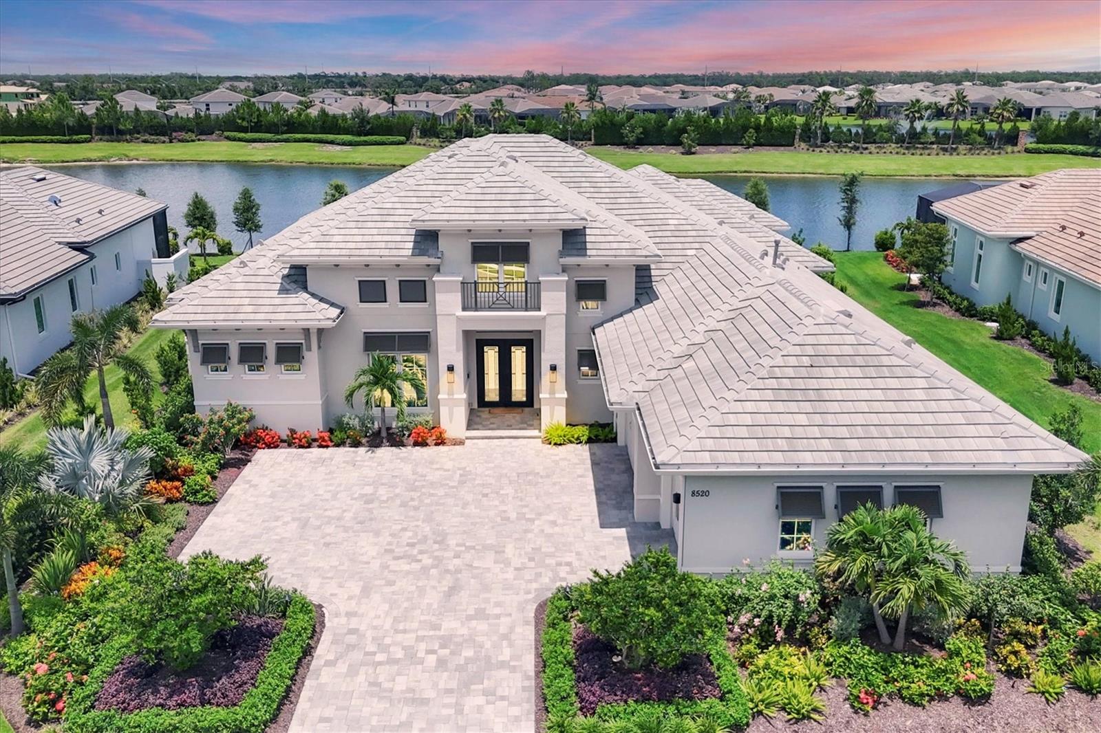 Welcome to the stunning Gardenia II model by Stock Signature Homes—where luxury meets livability in this impeccably designed 4-bedroom, 4.5-bath residence. Nestled on a prime lot with expansive water views and no rear neighbors, this home is a private tropical retreat from the moment you arrive. A pavered driveway and lush, manicured landscaping set the tone for what awaits inside. Step through elegant glass double doors into a bright, open-concept floorplan filled with natural light. Soaring ceilings, crown molding, neutral white oak engineered hardwood flooring, and designer finishes—including plantation shutters and tasteful draperies—create a warm and elevated atmosphere throughout. The spacious great room features a coffered ceiling, built-in shelving, and sleek floating shelves—perfect for entertaining or relaxing in style. The gourmet kitchen is a chef’s dream, with quartz countertops, soft-close white cabinetry, under-cabinet lighting, a large island with abundant storage, walk-in pantry, and Jenn-Air stainless steel appliances. The formal dining room just off the kitchen includes a dry bar with wine cooler and overlooks the serene pool area. Outdoor living is taken to the next level with an expansive travertine lanai, panoramic screens for uninterrupted water views, a saltwater pool and spa, and multiple covered spaces for lounging and dining. Entertain with ease at the outdoor kitchen—complete with grill, sink, beverage cooler, and a large island—or gather around the cozy outdoor gas fireplace. The luxurious primary suite is a tranquil escape with double tray ceilings, dual walk-in closets with built-in organizers, private lanai access, and a spa-like ensuite bath featuring dual vanities, quartz countertops, a free-standing soaking tub, large walk-in shower, and abundant storage. Each of the three additional bedrooms includes its own ensuite bathroom for comfort, as well as closets with custom organizers designed to maximize storage space. A bonus room with ceiling beams and sliding doors to the lanai offers versatility as a media room, gym, or fifth bedroom. A light-filled den with French doors and tray ceiling provides a perfect work-from-home space. Additional highlights include a powder room, a well-equipped laundry room with ample cabinetry and counter space, and a side-turned 3-car garage with extensive cabinetry. The state-of-the-art Control4 system seamlessly integrates the home’s audio/visual features, lighting, and security cameras—offering effortless smart home control at your fingertips. With hurricane impact windows and doors throughout, this exquisite home offers both peace of mind and timeless sophistication. Nestled in The Lake Club is an impressive 20,000-square-foot Grande Clubhouse, a hub of luxury amenities. Enjoy two pools, including a zero-entry pool with splash park, perfect for family fun. Indulge in poolside dining and unwind at the spa and fitness center offering guided workout classes, massages and facials by on-staff aestheticians. Sports enthusiasts will appreciate the tennis and pickleball courts with expert racquet pros available. Experience a vibrant social scene with a calendar filled with events. Inside the Grande Clubhouse, relax with billiards, pool tables, televisions, and game and card tables for various entertainment options. Don’t miss the opportunity to experience luxurious lakefront living at its finest.