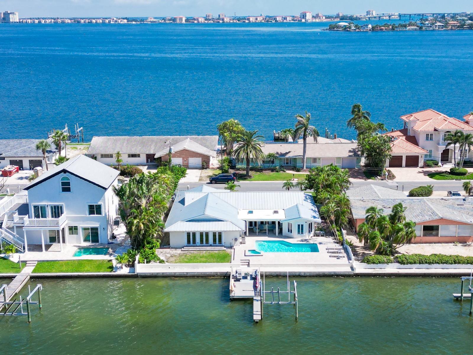 Welcome to your private waterfront oasis on Boca Ciega Bay, where panoramic water views, spacious open living, and modern European elegance come together in this beautifully furnished 4-bedroom, 3-bathroom home. Featuring a split floor plan, luxury vinyl flooring, and a brand-new custom kitchen with all-new high-end stainless steel appliances, wine cooler, warming drawer, and walk-in pantry, this home is designed for both comfort and style. The master suite offers a cozy sitting area, bay window views, and a spa-like en-suite with walk-in shower, travertine tile, and dual vanities. Three additional bedrooms and two updated baths provide space for guests and family, while multiple living areas, indoor laundry, fireplace, and French doors open to a tropical backyard retreat with heated pool, covered patio, dry bar, outdoor refrigerator, and designer furnishings—perfect for entertaining. A boat lift is available upon request. Ideally located just minutes from the beach, shopping, dining, Ft. De Soto preserve, and vibrant downtown St. Pete. Available for a minimum 7-month rental—just bring your toothbrush and embrace the Florida lifestyle with daily dolphin sightings and breathtaking sunsets.