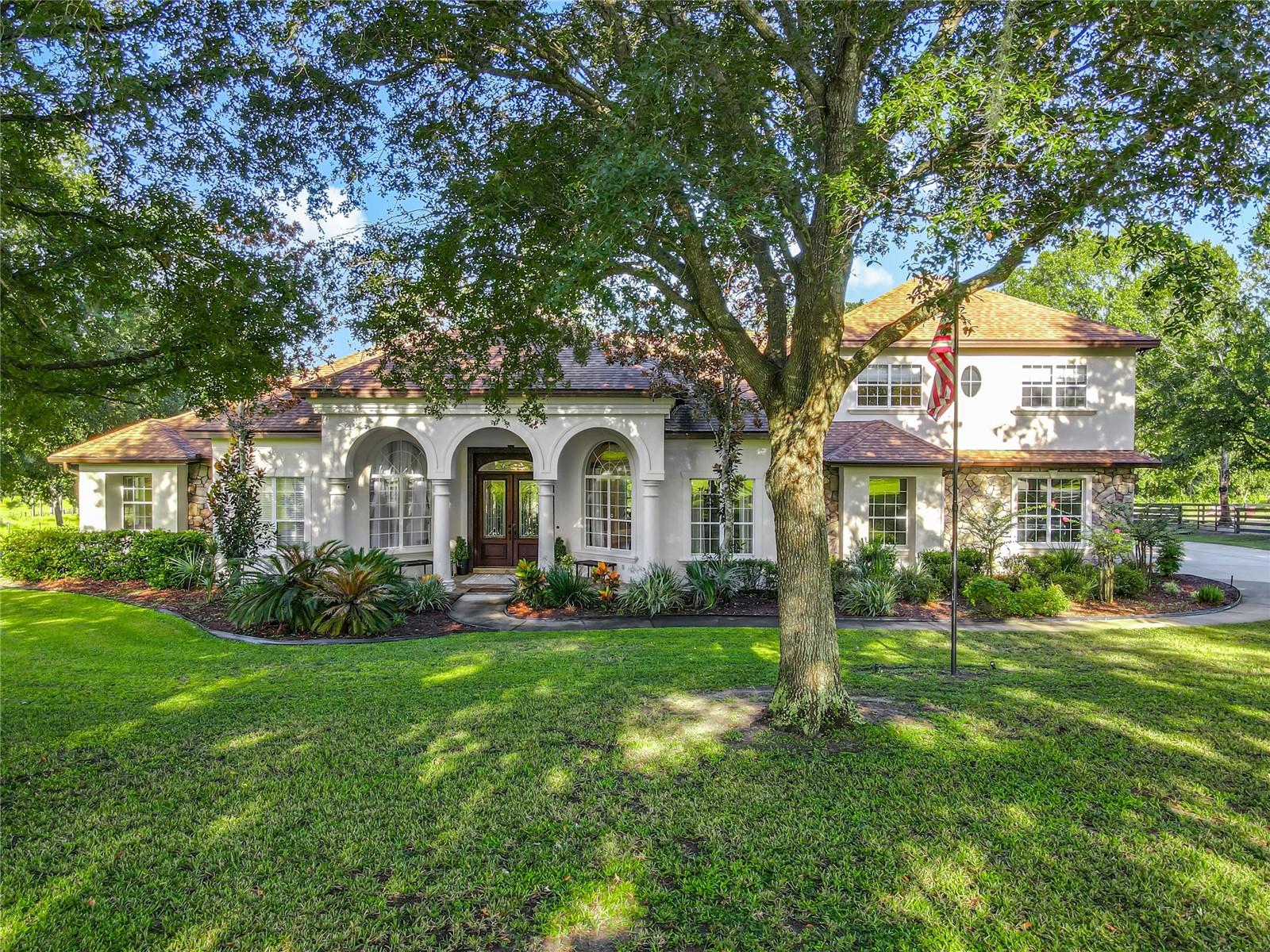 One or more photo(s) has been virtually staged. Waiting for you is this gated estate, where peaceful country living meets tasteful modern comforts. Tucked away on nearly 5 fully fenced areas with no HOA, this 3,760 square foot home is surrounded by lush landscaping and mature oak trees. Custom-designed this home features 4 bedrooms, 3.5 bathrooms, an office, and a theater room—all thoughtfully arranged within a spacious, light-filled open floor plan. Adding to the appeal is a 3-car attached garage, complemented by a 2-car detached garage with a dedicated gym area. The fully renovated kitchen features stunning quartz countertops, bar seating, stainless steel appliances—including a wine fridge—a sleek ceiling mounted range hood, and a spacious island. A large walk-in pantry with a built-in coffee bar adds both convenience and charm. Just off the kitchen, French doors lead to a generous second bedroom with an en suite half bathroom and private lanai access. Adjacent to the kitchen, the laundry room offers ample storage and direct access to the garage. Upstairs is a theater room and two additional bedrooms that share a Jack-and-Jill bathroom, creating a separate entertainment area for family or guests. The impressive primary suite highlights a large, custom walk-in closet filled with natural light, a generous sitting area, and French doors that open directly to the lanai. The inviting en suite bathroom includes dual sinks, a garden tub, a walk-in shower, and a private water closet. Conveniently located on the same wing is an office with a Murphy bed and a full bathroom, offering privacy and flexibility. Experience the peacefulness of the outdoors from the privacy of the screened lanai, complete with paved flooring and plenty of space to relax. The pool has a soothing waterfall, creating the perfect backdrop while you soak in the sun or take in the breathtaking, vibrant sunsets. Just beyond the lanai is a dedicated sports court perfect for playing pickle-ball and basketball. The property is fully fenced, with a separately fenced pasture that includes a shed row and livestock shelter. Conveniently located near the 429, you can enjoy easy access to everything Central Florida has to offer. Locally, you're just minutes from downtown Mount Dora, the Chain of Lakes, veterinarian clinics, feed stores, and retail shopping – yet you’ll be living on a property so peaceful, the hustle and traffic feel like a distant memory. This unique blend of convenience and tranquility lets you experience the best of both worlds every day. Schedule your private showing today!