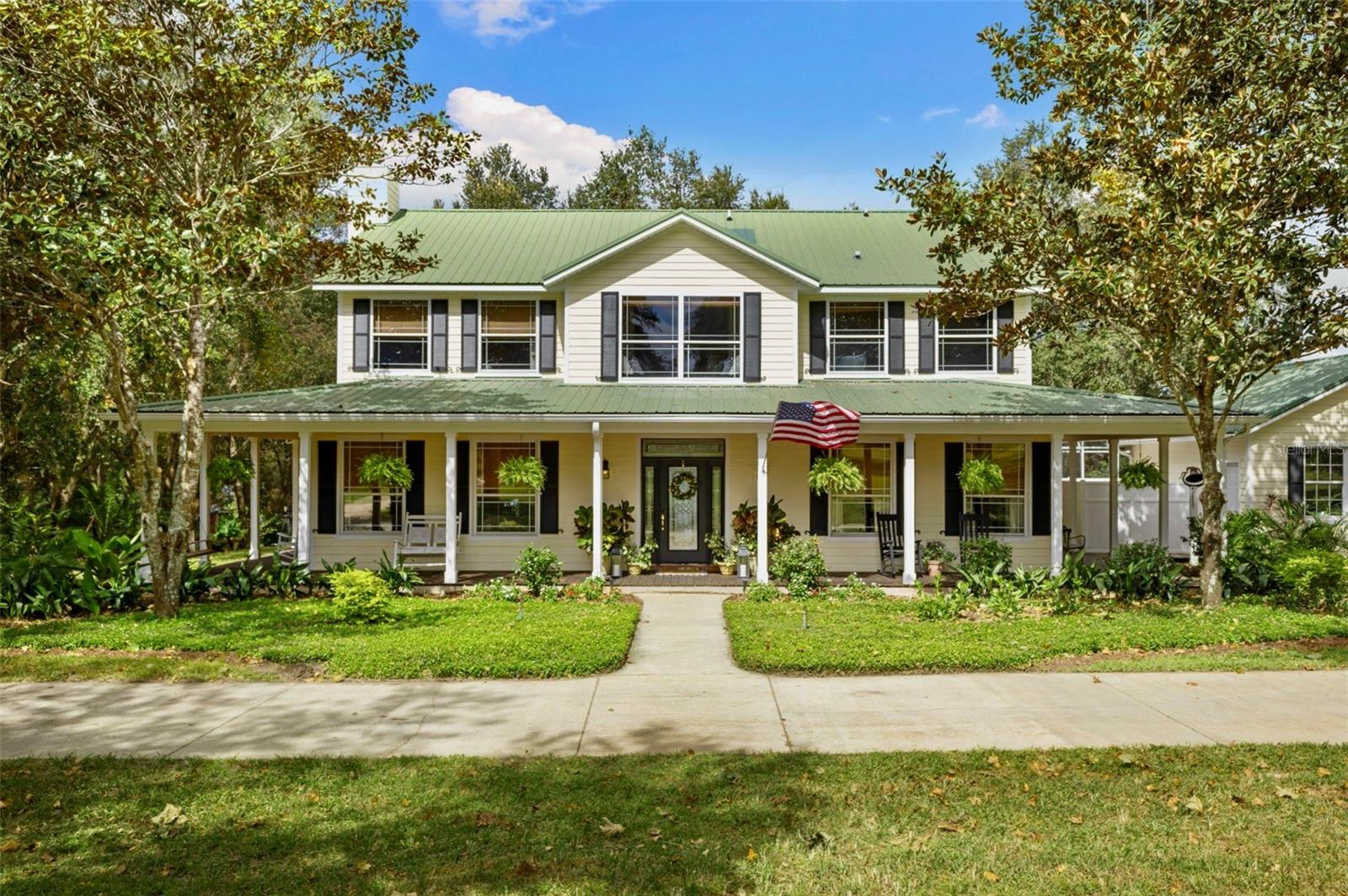 Experience peaceful, acreage living on nearly five acres at this lakefront modern farmhouse in Groveland. Surrounded by horse farms and open land, the property offers direct access to equestrian trails right from the front of the home. Built and carefully maintained by the original owner, the home features hardwood floors, tongue and groove ceilings on the wrap-around porches, and multiple indoor and outdoor areas ideal for gathering. All 5 bedrooms in the main house are located upstairs, including a primary suite that overlooks the lake and spacious backyard and features its own private balcony. The screened-in pool offers a quiet retreat, while the layout downstairs lends itself well to entertaining. This property includes 149 feet of frontage on skiable Indian House Lake, along with an 840SF barn dominium complete with its own bedroom, bath, kitchenette, and loft—ideal for guests or storage. A two-stall barn, detached garage, and open grounds make the property equestrian-friendly. Located just two miles from the Florida Turnpike, it offers a quiet setting with easy access to Clermont, Orlando, and Ocala. No HOA.