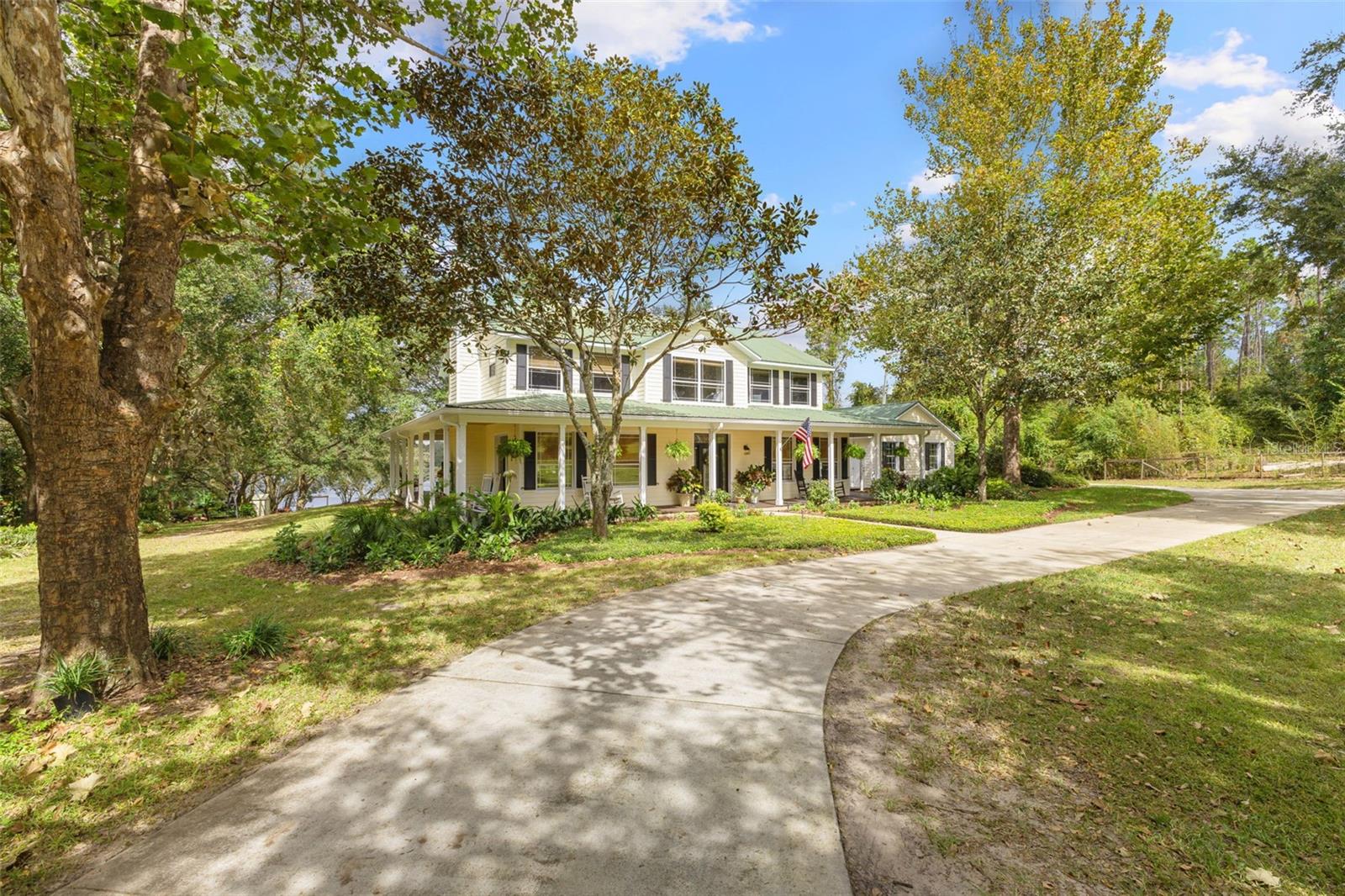 Experience peaceful, acreage living on nearly five acres at this lakefront modern farmhouse in Groveland. Surrounded by horse farms and open land, the property offers direct access to equestrian trails right from the front of the home. Built and carefully maintained by the original owner, the home features hardwood floors, tongue and groove ceilings on the wrap-around porches, and multiple indoor and outdoor areas ideal for gathering. All 5 bedrooms in the main house are located upstairs, including a primary suite that overlooks the lake and spacious backyard and features its own private balcony. The screened-in pool offers a quiet retreat, while the layout downstairs lends itself well to entertaining. This property includes 149 feet of frontage on skiable Indian House Lake, along with an 840SF barn dominium complete with its own bedroom, bath, kitchenette, and loft—ideal for guests or storage. A two-stall barn, detached garage, and open grounds make the property equestrian-friendly. Located just two miles from the Florida Turnpike, it offers a quiet setting with easy access to Clermont, Orlando, and Ocala. No HOA.