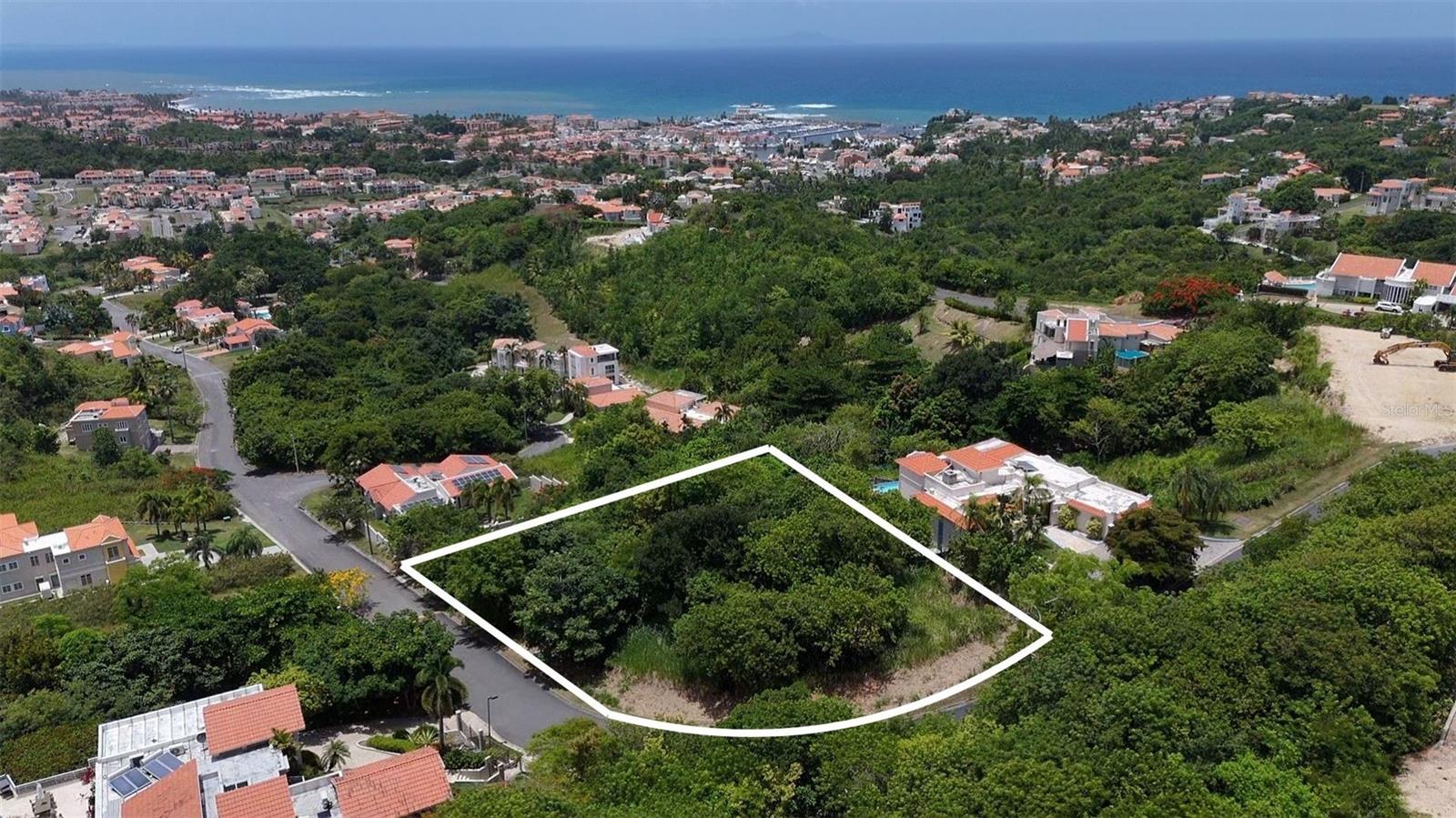 Discover the perfect canvas for your dream home at Harbour Lights 22 in Palmas del Mar Resort. This expansive 2,589 m² corner lot is perched on one of the highest elevations within the community, offering unobstructed panoramic views of the Caribbean Sea and the lush resort surroundings. With a gentle, build-friendly slope and a constant ocean breeze, this property is primed for a custom-designed residence that blends luxury with island living. Located in a private, gated enclave, this homesite not only offers privacy and dramatic vistas—it also grants access to the unmatched lifestyle that defines Palmas del Mar. Residents enjoy over two miles of beach, a 60-acre tropical forest, equestrian center, two championship golf courses, tennis and pickleball courts, a world-class marina, restaurants, bilingual school, and miles of golf cart paths connecting it all. Whether you envision a modern retreat or a timeless coastal villa, this lot delivers the space, setting, and resort amenities to bring your vision to life.