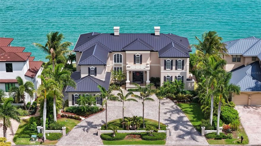 Set along the deep-water shores of Bird Key, this direct bayfront estate is a striking architectural achievement designed by renowned architect Cliff Scholz and constructed to exceptional standards by luxury builder Murray Homes. Spanning nearly 6,600 square feet of elevated living space, the residence captures panoramic Sarasota Bay views that stretch out to the Gulf while blending timeless craftsmanship with extensive recent updates and resort-inspired outdoor living. Positioned behind manicured landscaping and a pavered circular drive, the home makes a grand first impression with its stately facade, three-car side-entry garage, and elevated waterfront setting. Inside, luxurious finishes define the two-story interior, including cathedral and coffered ceilings, four-piece crown molding, solid-core doors, custom built-ins, cherrywood flooring throughout, chic lighting fixtures, and oversized impact-rated windows and French doors that fill the residence with natural light and sweeping water views. Recent improvements include a new metal roof (2024), rebuilt dock, newer seawall and lift, resurfaced pool, fresh interior and exterior paint, new landscaping, updated exterior lighting, three new garage doors, whole-house lighting, and a new Kinetico water treatment system. A statuesque foyer entry opens to the formal living room, where a stone gas fireplace flanked by custom built-ins serves as the focal point. Walls of floor-to-ceiling French doors seamlessly connect the interior to the expansive outdoor entertaining areas overlooking Sarasota Bay. The formal dining room is complemented by nearby built-ins and a wet bar. At the center of the home, the gourmet chef’s kitchen features marble flooring, contemporary custom cabinetry, professional-grade Viking appliances including a six-burner gas range, double ovens, and Bosch dual dishwashers, along with an oversized island, breakfast bar, and informal dining area. An oversized walk-in pantry with additional wine refrigeration and a first-floor laundry room complete this thoughtfully designed culinary space. To the West, the family room offers en-suite bath access, and a walk-in closet—allowing flexibility as an additional guest suite if desired. A private study completes the main living level. The second floor is devoted to family and guest accommodations and can be accessed by either the elegant solid-wood staircase or private two-stop elevator. Upstairs, a media room and second laundry room enhance everyday convenience, while the bayfront primary suite serves as a luxurious retreat with walls of glass framing spectacular water views and access to an expansive terrace overlooking the bay. The en-suite bath is a spa-like sanctuary featuring extensive custom cabinetry, dual vanities, dedicated makeup area, soaking tub, large glass-and-tile shower, and private water closet. Three additional guest suites are positioned privately along the western wing of the home, each offering walk-in closets, en-suite baths, and one with direct terrace access. Outdoor living is equally exceptional. The multi-level bayfront entertaining areas include an expansive covered terrace with built-in grilling station, lounge and dining spaces, heated swimming pool, and direct boating access—creating an ideal environment for boating enthusiasts and waterfront entertaining alike.
Located within the coveted Bird Key community, residents enjoy a prime Sarasota address between downtown Sarasota and St. Armands Circle.