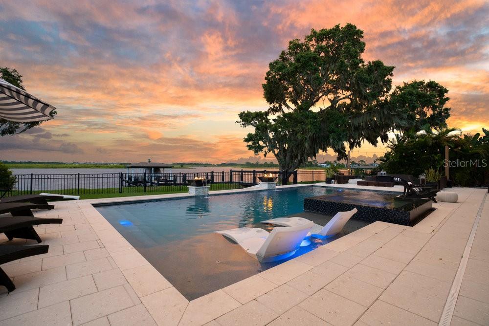 Stunning Lakefront Estate on Emerald Pointe Island – Hickory Hammock. Welcome to one of the most exclusive properties in the gated community of Hickory Hammock, located on the exclusive island of Emerald Pointe, one of very few island communities in Central Florida. Tucked securely behind two private gates and nestled on the shores of John’s Lake, this extraordinary lakefront estate offers unmatched sunrise and sunset views from both the front porch and the expansive backyard. Set on nearly half an acre, this 5-bedroom, 4.5-bathroom home includes an office, loft, and a media/game room—providing almost 5000 square feet of thoughtfully designed living space. The home is energy-independent, powered by a **fully paid-off solar system**, and built for luxurious Florida living. Step outside to your private dock with a boat lift perfect for boating, fishing, or simply relaxing on the lake. Enjoy the custom heated pool and spa, all controlled with automated smart technology. The outdoor living space also features a **fully equipped summer kitchen** with a grill, dual refrigerators, sink, and ice maker perfect for entertaining. The backyard is fully fenced and also features artificial turf for easy, effortless maintenance. Inside, you'll find custom woodwork throughout, including crown molding, built-ins, and detailed window casings. The primary suite is a true retreat, featuring a custom fireplace, private lakefront balcony, and designer walk-in closets. The upstairs loft is wired for surround sound and includes a projector, making it an ideal home theater. Additional highlights include a 4-car garage with enhanced storage, an over sized drive way accommodating 6+ cars, a large upper-level balcony, and plenty of indoor and outdoor space to enjoy serene lakeside living. Don’t miss this rare opportunity to own a true gem on John’s Lake with luxury, privacy, and views in every direction.