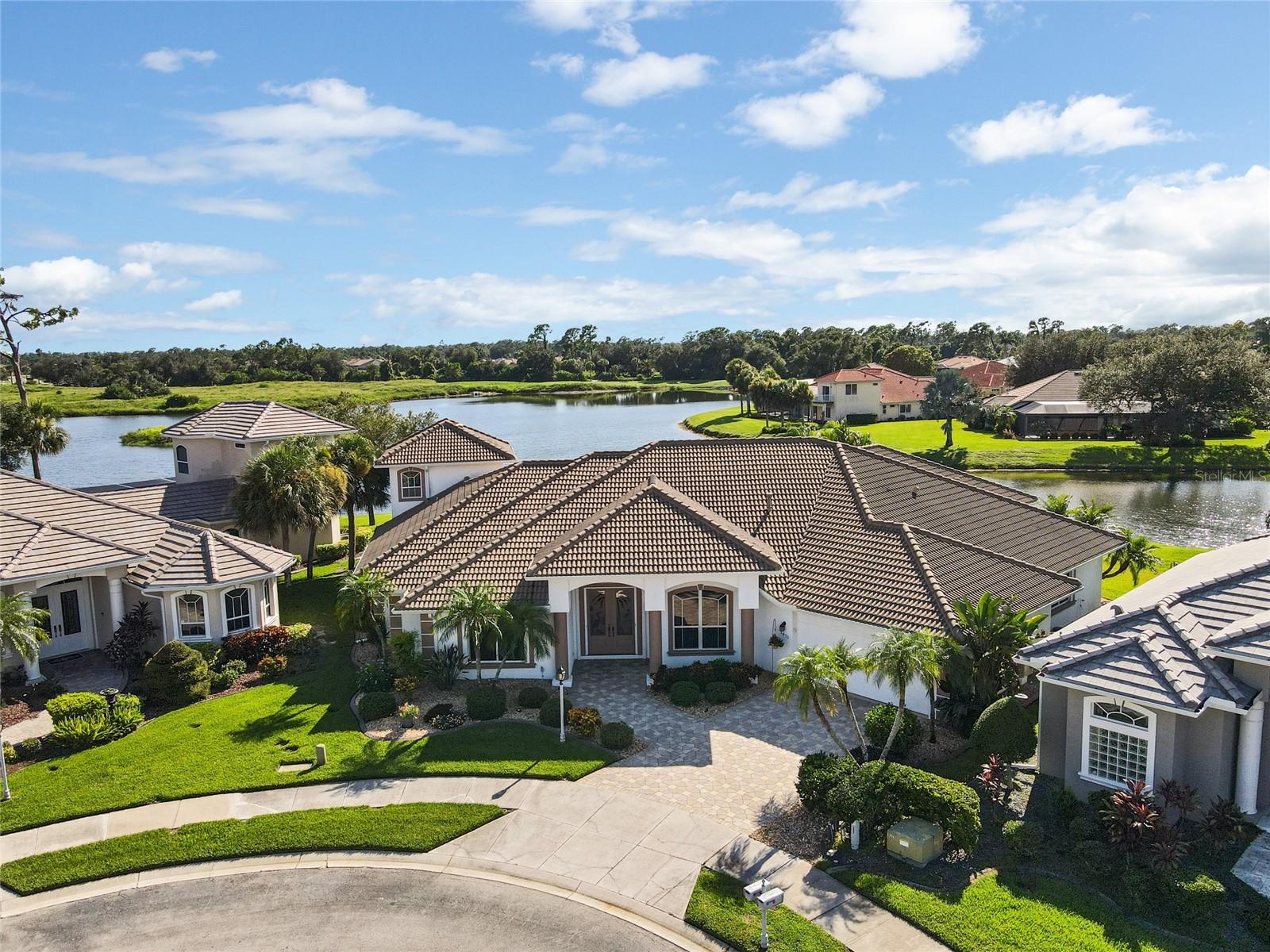 Welcome to this custom-built, one-owner estate in the gated community of Bobcat Trail, where thoughtful design and unexpected surprises make this home truly extraordinary. From the street, it appears as a handsome, well-kept residence—but step inside, and you’ll discover it’s the “Superman” of homes, offering an abundance of space, style, and luxury.
Behind the double front doors, you’re greeted by a grand foyer with 12-foot ceilings, crown molding, and abundant natural light pouring in from zero corner sliders framing stunning views of the pool and lake. Western exposure keeps the home bright throughout the day, while evening brings a glow from elegant uplighting and dimmable fixtures. The formal dining room features a built-in china hutch with glass doors, while the living/bar room leads to the kitchen and master wing on one side and the guest wing on the other.
The kitchen offers cabinets galore, solid surface counters, a prep sink, and easy flow to the family room with its gas fireplace, wet bar, beverage fridge, and ice maker. The office includes a built-in desk and sliders to the lanai, while the primary suite features lanai access, dual vanities, a garden tub, walk-in shower, and a massive custom closet with shelving and cabinetry. The laundry room is equally functional with washer/dryer, upright freezer, and built-in ironing station. A half bath serves guests.
The opposite wing of the home hosts two guest bedrooms and two full baths, plus a game room with sweeping lake and pool views. Upstairs, a fourth bedroom—currently a home gym—offers the best vantage point of all.
Outdoor living takes center stage on the expansive lanai, featuring a resort-style pool with fountains, table and stools, an 8-person spa, and a full outdoor kitchen with bar, sink, and full-size fridge. A motorized awning gives you the choice of sun or shade.
And the surprises don’t stop there: the garage, which looks like a standard 2-car from the front, is actually a 3+ car garage with room for golf carts and a workshop.
With its combination of luxury, livability, and unmatched storage, this home is a rare gem in one of North Port’s most sought-after communities.