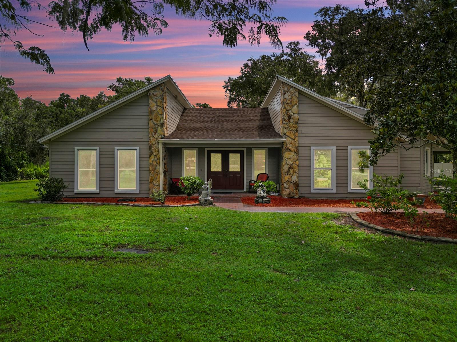 Discover the perfect blend of sophistication and tranquility in this custom-built residence, set on 2.15 acres of beautifully maintained, fenced pastures with no HOA or CDD. A private paved drive leads to a home where timeless craftsmanship meets modern amenities, featuring a chef’s kitchen with premium stainless-steel appliances including a gas range, abundant cabinetry, spacious island with wine refrigerator, and a $2,000 seller credit toward the buyer’s choice of refrigerator. The dining room is separated from the family room by a see-through gas fireplace, while vaulted ceilings, built-ins, wet bar, recessed lighting, ceiling fans, and vinyl flooring create a welcoming space for entertaining. Recent updates include a new roof (2025), fresh interior and exterior paint, serviced well with new bladder and 5-year warranty (2024), serviced septic (2024), and new A/C (2025) with 10-year warranty, plus an additional electric unit under a 5-year warranty. Gas appliances include the stove, dryer, A/C, water heater (2020, 15-year warranty), and fireplace. Outdoors, enjoy a brick-paved courtyard with built-in grill, bar, and fire pit, a pole barn with two horse stalls, cross-fencing, pond, and multiple carports ideal for vehicles, RVs, or toys. The garage offers a workshop with electric, and 50-amp service, perfect for a motorhome. The property is regularly serviced by a pest control company and provides ample space for livestock, hobbies, and gatherings under the stars—all while being just minutes from dining, shopping, and major highways.