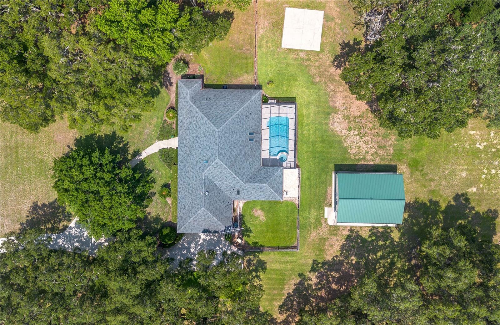 Discover an exceptional blend of luxury, privacy, and functionality on 4.20 acres in the sought-after, gated community of Alamar Village. This meticulously designed 5-bedroom, 4-bath estate spans 3,498 square feet and offers a flexible split-bedroom layout ideal for both everyday living and elegant entertaining. Set back from the road, mature landscaping and grand oak trees set the tone for this peaceful retreat. Inside, engineered wood flooring extends throughout the main living areas, with tile in the kitchen and baths. The heart of the home is the central living room which features a custom built-in entertainment center and French doors opening to the expansive pool area. The oversized kitchen is designed for those who enjoy cooking, featuring a center island, gas range, breakfast bar, wine rack, generous cabinet storage, and a walk-in pantry. A cozy breakfast nook with built-in bench seating overlooks the pool, while the formal dining room off the foyer and kitchen adds a touch of sophistication for hosting. A versatile library with extensive built-in shelving, a walk-in closet, and private full bath offers the perfect space for a home office, guest suite, or quiet reading room. The primary suite is a private haven with dual walk-in closets and an ensuite bathroom featuring dual vanities with under-lighting and a large walk-in shower. The lifestyle continues outdoors with a resort-style saltwater pool and spa surrounded by travertine decking and enclosed with a new screen cage. Enjoy shaded relaxation under a covered area with ceiling fan, an ideal for gatherings or quiet evenings that even includes an outdoor sink for added ease. Beyond the pool, the backyard is fenced with no-climb and board fencing and includes a separate patio area. Additional highlights include a utility hallway with extensive built-in storage, laundry area, and an extra refrigerator; a side-entry attached garage; and a multi-functional Morton building offering a 12’ x 28’ insulated room, 4-car garage, patio, and RV stall with electric hookup (per HOA, RVs may not be stored outside). Set in a tranquil, equestrian-friendly setting near Ocala’s Florida Horse Park and the Cross Florida Greenway’s expansive trail systems, this property offers space, serenity, and sophistication– perfect for those seeking a luxury lifestyle with room to live and breathe!