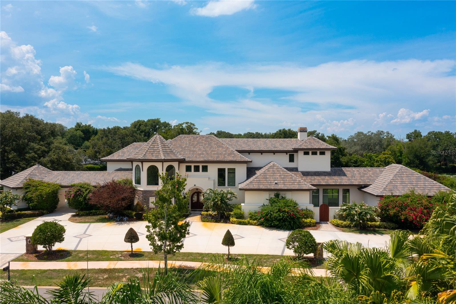 This splendid custom-built, Tuscan-style pool home is located in the highly sought after gated community, Chaine Du Lac in Windermere. It sits on a 1.06-acre lot and offers 6000 square foot of living space with 4 bedrooms, 5 full bathrooms. Entering the home through the exquisite solid wood arched doors, you’ll be greeted by 15-foot ceilings and a stunning view of the back patio and pool through ceiling to floor windows. You’ll instantly notice the craftsmanship and expert care that went into the custom carpentry and crown molding details throughout. The first floor consists of a guest suite with a private entrance and an ensuite that is shared with a spacious and well-equipped movie room with brand new carpeting and fresh paint. There’s even a 1-car garage, attached by a breezeway, offering easy access to the guest suite. You’ll also find another full bathroom and a convenient drop space leading from the 3-car attached garage, complete with EV charger. This thoughtfully designed floorplan showcases an open-concept kitchen and family room as the heart of the home. The gourmet kitchen exemplifies culinary sophistication featuring two center islands. One island features beautiful, chiseled edge granite while the other boasts double stacked granite with beveled edges. You’ll enjoy a Thermador Convection Steam oven, Wolf refrigerator/freezer, large walk-in pantry and more than enough counter and storage space. An alternative staircase leading to the second floor creates easy access for those mid-night snacks. Just outside the kitchen is a dedicated area for growing all your own vegetables for fresh “garden to table” meals. The wine closet showcases a mural that takes you right into the wine country of Italy. The expansive family room present an inviting transition to the spacious screened outdoor living space through massive accordion glass doors that seamlessly blends indoor and outdoor living. The outdoor living is made easy with automatic screens and a fully equipped outdoor kitchen for hosting those relaxing dinners with friends and family. Beyond the screened area is a large patio and brand-new pool. The massive, tree-lined, fenced back yard offers more than enough space for you to use your imagination!
Back inside, when you ascend the stunning grand staircase to the upper level, you’ll find two additional bedrooms with private ensuites and walk-in closets. An extra spacious laundry room with plenty of counter and cabinet space is centrally located on the second floor. Beyond the laundry room, up another short flight of stairs, is a flex space just before entering the magnificent primary suite that could be used as an office or workout space. The primary suite features a gas, double sided fireplace, built-in shelving and is adjacent to a spa like ensuite featuring a large walk-in shower, separate soaking tub, dual vanities, and walk-in closet.
This home boasts architectural details and exquisite finishes throughout and signifies the essence of sophistication and luxury, lacking none of the convenience of modern technology as 85% of the home can be controlled with your phone.