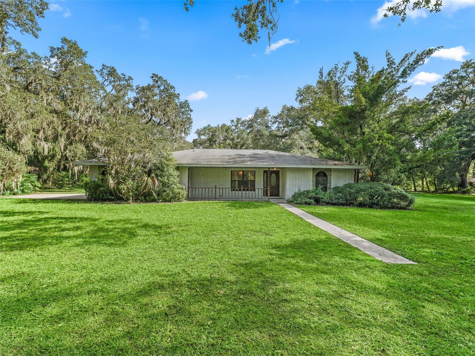 This property features four bedrooms and three bathrooms, situated on five picturesque acres shaded by majestic oak trees. It is conveniently located near major highways, restaurants, shopping centers, and medical facilities, offering both tranquility and easy access to amenities. Upon entering the home, you are greeted by a large picture window that showcases stunning views of the property. The spacious floor plan features the primary bedroom on one side and three additional bedrooms on the other. The primary bedroom includes two closets and an en-suite bathroom with dual sinks, while the other bedrooms are generously sized, providing ample space for comfort. In the kitchen, you'll find an abundance of counter and cabinet space, along with a pantry for extra storage. There is a pass-through window leading to a screened porch with a bar, making it perfect for entertaining guests. The eat-in kitchen and formal dining room ensure plenty of room for gatherings. Additionally, the property includes a 2-car garage and an extra parking pad for your convenience. With all these features, this property is ready for you to bring your vision to life. Come and take a look—you won’t regret it!