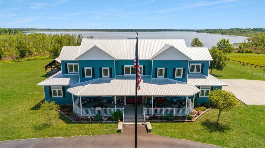 Welcome to a rare opportunity to enjoy lakefront living and equestrian luxury on 19.96 acres of beautifully improved land in Ocklawaha. Nestled beneath a canopy of grand oaks, this gated estate is set on the shores of Lake Bryant—one of Central Florida’s largest recreational lakes—offering unmatched natural beauty and privacy. With over 5,500 sq ft in the main home, a detached two-story guest apartment, multiple garages and barns, a 3-bay metal building, and a private dock with beach access, this property offers space, functionality, and lifestyle in one stunning package. The country-style main home features warm, rustic finishes and spacious living throughout. The downstairs primary suite includes a walk-in closet and spa-like bath with clawfoot tub, walk-through tiled shower, and dual vanities. Also on the first floor is a private office with French doors and built-ins, a large laundry room with a Murphy bed, utility sink, and extra storage, plus a separate storage room. Wood-look tile flows throughout. The kitchen offers abundant cabinetry, granite counters, a ceramic farmhouse sink, gas cooktop, double ovens, a blue-accent island, and a large walk-in pantry. The dining area overlooks the backyard and lake through oversized windows. Upstairs, two large bedrooms each include private bathrooms, with one offering a game room. A central loft overlooks the open-concept living room below, designed for comfortable everyday living or entertaining guests. Outside, a covered cabana includes a granite summer kitchen with gas grill, TV, dining area, hot tub, and wood-burning fireplace. Just beyond, enjoy your own sandy beach and private dock with lakeside gazebo and a covered swing—ideal for fishing, tubing, or peaceful waterfront relaxation. Equestrian amenities include a newly constructed 4-stall barn with room for 4 additional stalls. Four stalls have run-outs to a large fenced pasture. The barn includes a full bathroom, air-conditioned tack room, feed room, and an elegant rustic chandelier—perfect for events. A lean-to with a concrete floor offers added space, including a wash rack and enclosed, air-conditioned garage. Additional features include two large pastures, matching chicken coop, 2-stall wooden barn, 2-stall loafing shed, round pen, and several fenced paddocks. For storage and workshop needs, the property includes a massive 4-car metal garage with full-length carport, a detached 2-car garage with carport, a separate equipment building, and a 3-bay metal building providing additional covered parking or storage for trailers and implements. The detached guest apartment offers two bedrooms, two bathrooms, a full kitchen, living area, upstairs window overlooking the garage, and a private front patio—perfect for guests, family, or rental use. Located just 20 minutes from shopping and dining in Ocala, 25 minutes to the Florida Horse Park, and under 45 minutes to the World Equestrian Center, this one-of-a-kind estate combines waterfront serenity with equestrian functionality—no HOA, no deed restrictions.