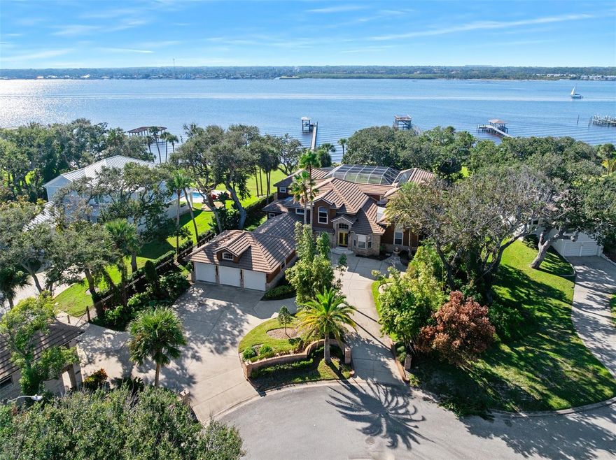 Fabulous waterfront estate home perched high on a bluff offering commanding views of the intracoastal waterway across the beautiful oak shaded riverfront lawn. With almost 8000 Sq Ft of high end custom construction, the home is situated on nearly 1 acre of elevated land and offers a 5 bedroom, 4.5 bath main home in addition to a detached 1 bed, 1 bath waterfront guest house and a 6 car garage. Enter the home to find a tremendous waterfront great room where multiple living, dining and entertaining spaces flow together seamlessly under volume ceilings while enjoying panoramic water views. A series of French doors open onto the fabulous screened paver appointed lanai that surrounds the crystal blue pool and serves as the ultimate area to entertain or relax with a grand poolside wet bar, dedicated pool bath, dry sauna and firepit. The custom home is truly one of a kind with a magnificent ground floor owners' suite with a private waterfront den with fireplace, cavernous walk-in wardrobe and a fantastic bath with double vanities, jacuzzi tub and steam shower. Eat-in island kitchen opens into the great room and is just adjacent to the lovely formal dining room with a gas fireplace. A handcrafted solid wood wine bar is just off the stately dining room and just steps from the poolside patio. A choice of two staircases will carry you to the second floor where three bedrooms and multiple open air lofts and landings await with panoramic views of the water and the rolling green lawn. The magnificent waterfront grounds below the elevated pool deck features a fabulous gazebo centered between towering live oaks. A concrete pathway stretched to the base of the deepwater dock with a sun deck, boat house w/lift and second story observation level above. The unique lot is situated at the end of a quiet cul-de-sac and allowed space for the longtime owner to construct a lovely guest quarters atop a seperate 1.5 car garage with a waterview living room, bedroom and balcony. Two more connecting oversized showroom garages with a total of 5 large spaces are ideal for the collector finished with tile floors and gracious windows for plenty of natural light and breezes while tinkering. The home has been outfitted with a Generac generator. A new 50 rear tile roof was installed in 2018. The quiet location contributes to the undeniable serenity. Sit beneath the oaks and watch the sunset while you listen to the Atlantic Ocean crash the shore from just two blocks away. Jump in your boat and be on Ponce Inlet's Disappearing Island in mere moments or tie up to the dock at Down the Hatch Seafood to listen to live music and enjoy a fish sandwich. This property has been consistently maintained by a knowledgeable longtime owner who is market savvy and has priced this for immediate sale.