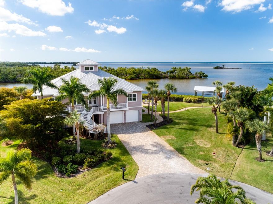 This custom-built waterfront home is positioned along the shoreline of Charlotte Harbor in Charlotte County. The residence sits on an estimated 275 feet of direct Saltwater, providing open water access and expansive views across Charlotte Harbor. The southwestern exposure allows for consistent natural light across the water during afternoon and evening hours. Constructed in 2013 by West Coast Builders, the home is supported by 38 concrete pilings driven approximately 12 feet deep. Exterior construction includes Hardie Board cement siding along with impact-resistant windows and doors throughout. The structure was designed with durability in mind and includes provisions that allow for a future elevator installation if desired. The property is accessed by a paver driveway bordered by mature tropical landscaping. Double front entry doors open into the main living area, with an open floor plan, and ceiling heights range from approximately 10 to 12 feet, including an 11-foot double-step tray ceiling. Light walnut-toned porcelain tile flooring extends throughout the primary living spaces, providing continuity and suitability for a coastal environment. The living room is oriented toward the water and features a built-in solid-wood entertainment center designed to conceal electronic components. Large windows throughout the home maintain a visual connection to the surrounding harbor setting. A built-in window seat is positioned between dual French doors that lead to two elevated open-air decks overlooking Charlotte Harbor, providing outdoor living space with wide water views. The large kitchen features a functional layout with modern finishes. Euro-style flat panel cabinetry in a dual-tone finish is paired with Oakhampton Cambria quartzite countertops. A central island includes a prep sink and ample drawer storage. Appliances include a 36-inch Wolf gas cooktop, a wall-mounted oven, and a convection microwave. An expansive walk-in butler’s pantry offers additional workspace and storage. The primary suite is a true oasis, with 8' sliding glass impact doors leading to a private deck with unobstructed views of the harbor. Dual custom walk-in closets and a linen closet provide ample storage. The Ensuite bathroom includes a soaking tub, a walk-in shower with multiple shower heads, a floating vanity with dual sinks, and a water closet. Situated off the kitchen is the guest wing, which consists of two bedrooms with built-in closets, one of which features sliding glass doors leading to the shared deck with expansive water views. The large full bathroom with a walk-in shower and linen closet completes the guest amenities. The main floor also includes a laundry room with a front-loading washer and dryer, plenty of cabinet space, a refrigerator, and a dumbwaiter, which makes bringing groceries upstairs a breeze. Outdoor amenities include a saltwater swimming pool, a heated spa, and a waterfront fire pit area. Shoreline improvements consist of a private tiki hut, dock, covered boat lift, and kayak launch. These features support direct access to Charlotte Harbor and accommodate boating, fishing, paddling, and other water-based activities directly from the property. Additional features include a three-car tandem garage with a dumbwaiter, multiple storage areas, a climate-controlled hobby room, a half bathroom, and an outdoor shower. .