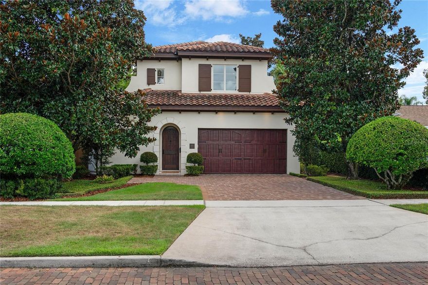 Located in the coveted Tree Streets just a block and a half from Lake Knowles, this timeless Mediterranean home offers three bedrooms, three and a half bathrooms, and just under 2,000 square feet of beautifully finished living space framed by mature magnolias and manicured hedges. A brick driveway leads to a two-car garage with carriage-style doors, while a covered entry showcases a solid arched wood front door with classic peep hole, setting the tone for the craftsmanship inside. Step through the entry and discover a hidden laundry room with dark wood cabinetry, marble countertops, subway tile backsplash, and front-loading washer and dryer, along with a sophisticated powder bath featuring a floating marble-topped sink, wall-mounted chrome faucet, integrated mirror lighting, and detailed molding. Just beyond is a flexible room that functions as a dining room or formal living space, and through the next doorway the home opens to a large kitchen and great room designed for everyday living and entertaining. The kitchen combines dark wood perimeter cabinetry with accent glass fronts, a creamy white island with storage on both sides, marble countertops, and stainless appliances including a GE Monogram gas cooktop with vent hood, convection oven, refrigerator, dishwasher, and LG under-counter microwave, all anchored by a deep single-barrel undermount sink with extendable faucet. The great room features a gas fireplace with mosaic tile surround, clerestory windows, extensive crown molding, and hardwood floors, with new Anderson French doors that open to the private backyard where brick decking frames a cocktail pool with water features by Signature Landscape, surrounded by mature greenery and magnolias. The primary suite, tucked on the back right wing, also enjoys French doors to the pool terrace and includes new carpet, a customized floor-to-ceiling walk-in closet, and a bath with travertine floors, sunken glass-enclosed shower with built-in shelving, creamy white vanity topped with marble, satin nickel fixtures, dual Kohler undermount sinks, and mirrored walls with crown molding. Upstairs, two spacious bedrooms each feature ensuite baths and customized closets—the front with a built-in desk, marble chicklet tile flooring, creamy cabinetry, and tub/shower combo, the second with a walk-in closet and a bath finished with travertine flooring, a slightly larger vanity with consistent cream cabinetry, marble top, and glass-enclosed shower. Additional highlights include hidden storage under the stairs, unique iron stair railing, 8’ solid wood interior doors, 10’ ceilings, and block construction, while recent updates such as an Italian tile roof (2020), newer garage door and opener, and new HVAC air handler provide peace of mind. Just a short walk to the YMCA, Phelps Park, and Interlachen Country Club, 1450 Chestnut Avenue combines Mediterranean charm, thoughtful updates, and a sought-after Winter Park location for a lock and leave lifestyle with ease.