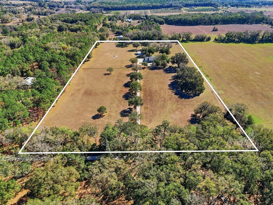 Welcome to your private retreat—a custom concrete block estate offering six bedrooms and three bathrooms, gracefully positioned on 20 breathtaking acres of mature oaks. Fully fenced and gated, this exceptional property delivers ultimate privacy and peace of mind while remaining conveniently close to town. A serene, tree-lined drive sets the tone as you approach, opening to a circular driveway and a welcoming front porch that invites you to slow down and stay awhile. Inside, the thoughtfully designed floor plan blends elegance with functionality. A formal dining room provides the perfect setting for gatherings, while a dedicated piano room or home office offers flexibility to suit your lifestyle. The spacious primary suite is a true sanctuary, featuring two walk-in closets, dual vanities, a jetted soaking tub, and private access to the screened pool patio—creating a seamless indoor-outdoor escape. On the opposite wing of the home, five generously sized bedrooms are filled with natural light and provide comfort and space for family and guests. The kitchen is designed for both daily living and entertaining, offering abundant cabinetry and a casual seating area for relaxed meals and conversation. In the living room, expansive glass sliders disappear into the wall, fully opening to the oversized screened-in pool patio and transforming the space into a grand open-air entertaining area you’ll enjoy year-round. A dedicated pool bath with direct patio access adds convenience for guests.
 Set atop a beautiful hill overlooking acres of rolling countryside, this property offers true country living with no HOA or deed restrictions. Additional features include a laundry room with exterior access ideal for use as a mudroom, a dedicated storage room, and a spacious 30x50 detached concrete garage providing ample room for equipment, recreational vehicles, tools, and hobbies. An RV hookup and additional septic tank add even more versatility. The seller has completed extensive improvements, including enclosing the garage to create two spacious bedrooms, fresh interior and exterior paint, new hardwood flooring and carpet, updated trim, a new dishwasher, new light fixtures, and a newly screened pool enclosure—ensuring the home is move-in ready. Despite its private, secluded, and peaceful setting, the property is just minutes from Alachua, High Springs, Gainesville, and Jonesville, with convenient access to University of Florida, HCA Florida North Florida Hospital, UF Health Shands Hospital, and Santa Fe College. This one-of-a-kind estate beautifully combines space, comfort, and accessibility. Private. Secluded. Quiet. Yet close to everything. A must-see property that truly captures the best of North Florida living.