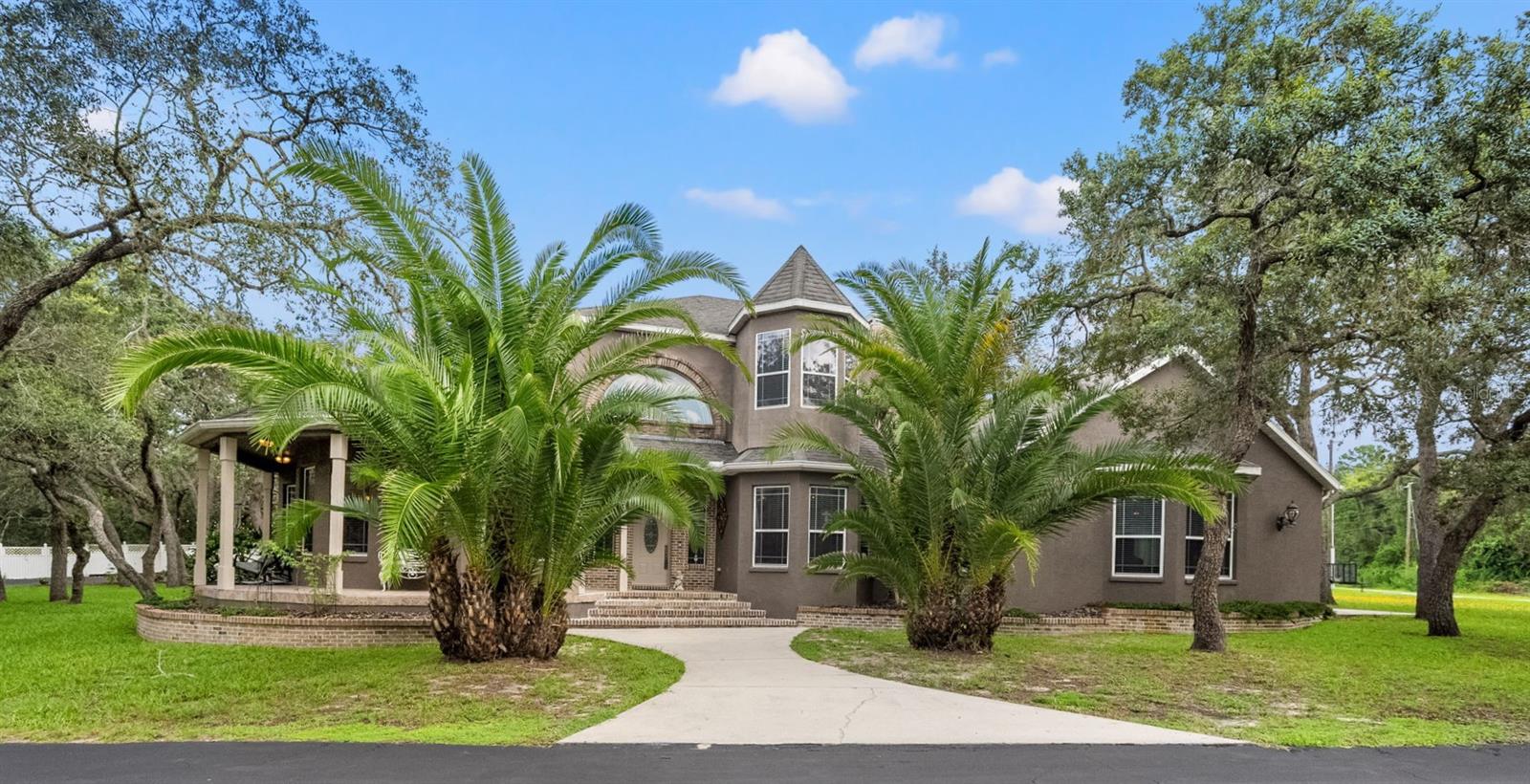 MOTIVATED SELLER! Elegant 3,500 sq ft custom home on 1.9 acres in rural Spring Hill. 3 beds, 3.5 baths, plus a 28x18 game room. Features soaring ceilings, hardwood/tile floors, turret-style rooms, grand staircase, and a chef’s kitchen with dual refrigerators, granite island, coffee bar, and custom cabinetry. The luxurious primary suite includes a spa-style bath and a walk-in closet the size of a bedroom. Enjoy the 1,050 sq ft screened lanai, charming wrap-around porch, RV hookups, dual driveways, and a peaceful setting just 11 minutes to the Suncoast Parkway. This home has hosted weddings and 100+ guest events—perfect for entertaining!