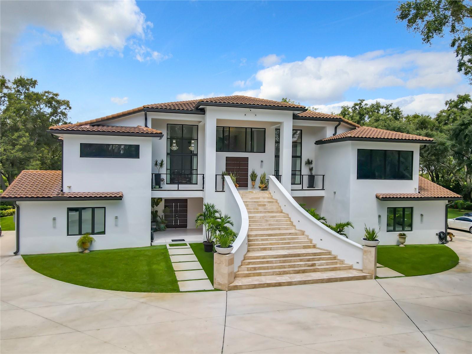 COUNTRY ESTATE LIVING AT ITS FINEST! It's easy to perfect the art of living when you live within a work of art. This stunning, custom-built modern pool home is perfectly situated on a premium 9.8 acre, privately gated homesite nestled in the peaceful country site of Groveland. Featuring 5 bedrooms and 5.5 baths, this 2-story rural estate offers 6,517 sqft under air living space and over 10,000 sqft under roof. Expect to encounter the very best luxury details & architectural craftsmanship in this state. Step inside through the grand double door front entry to an open concept gathering room with soaring full of detailed ceilings, imported Italian porcelain tile floors, amazing 20-foot glass wall, with views of the outdoor entertainment spaces, pool, and gardens. This chef’s dream kitchen is the heart of the home, and the open dining area is perfect for large gatherings. Featuring high-end stainless-steel appliances, the massive center island is the center of attention, fitting at least 8 chairs with a Miele cooktop, indoor electric grill, and griddle. The large walk-in pantry and trash compactor is ideal for busy households. The well-crafted custom-made wood cabinetry with crown moldings is accentuated by a rustica artisan sliding rack ladder boosting loads of storage at your fingertips. On the lower level, you’ll also find a half bath with pool access for your guests, three secondary bedrooms with in-suite bathroom, a game room, media room, Bar/Gym room with fully retractable sliding doors making this area a real party space. Back on the upper level, a separate home office with French doors and a gorgeous ceiling to floor glass wall makes long hours in the office go easier. The secluded primary suite features tray ceilings, wall to wall glass & an oversized sitting area that opens to the covered lanai, this is truly the owner’s private oasis. The spa-quality primary bathroom showcases a centerpiece soaking tub for 2, separate vanities, and a massive walk-in shower with dual showerheads and a relaxing rain shower above. This grand suite offers oversized, individual walk-in closets with custom organization systems. At the west wing you will find a full bathroom, kitchen, breakfast nook and family room all with amazing views of the pool area and gardens from its wrap around balcony. A spacious secondary bedroom with in-suite bath will also be found on this side of the house. Entertaining the outside presents limitless options on the covered patio for hosting friends & family. The oversized pool and hot tub will be a joy for your family and friends gathering. Enjoy the very best of the Florida lifestyle in a sparkling open-air pool. You’ll be impressed with the enormous interior laundry room and enough space for 2 additional full-size freezers/refrigerators. Vehicle storage is not a problem with a two 2-car attached garage “his & hers”, extended parking pad and an additional 2-story, insulated and stucco metal building with workshop to accommodate all your toys along with an attached large chicken coop for those morning fresh eggs. Located far enough to escape from the busy life, yet you are just a few minutes away from restaurants, school, shopping, a new hospital and the to be built Olympus City in Clermont. Among Million-dollar homes, this spectacular residence features upgraded landscaping & lighting, is fully fenced & protected by an automatic gate. Ah, did I mention these home features and safe room? Home is under surveillance.
