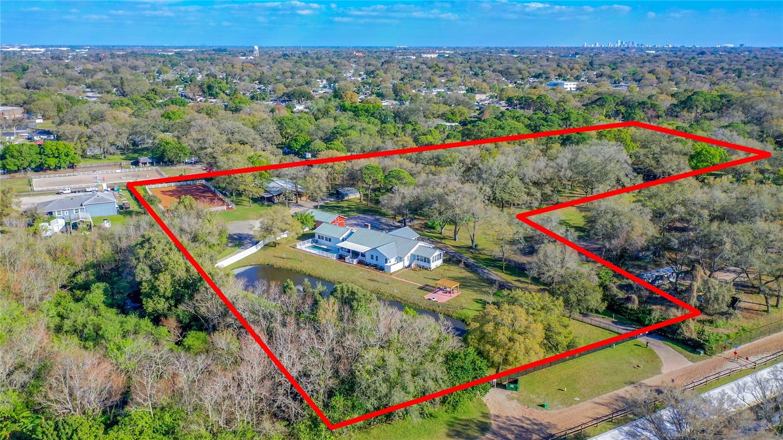 Under contract-accepting backup offers. The most unique and tranquil property in Pinellas Park! This 6 acre estate comprises multiple structures including a 10-stall income producing horse stable, a barn with two additional minature horse stalls, office & hay loft, and a 3,161 sqft single-family fully furnished home with a great history! This spacious farmhouse was built in 1900 by the Belcher family who were pioneers in the Pinellas area. The home originally sat on Belcher Rd (named for the same family) and in 2002 its floor joists were carefully reconstructed and reinforced so that the home could be moved to its current location on this estate that borders the Pinellas Park Equestrian Trail & Helen Howarth Park & Equestrian Center. This property’s proximity to the equestrian trail makes it like none other you will find and allows you to ride directly from the stables only a few hundred feet and cross the property line where you can enter the trail or arena. The grounds of this estate have been beautifully enhanced by the current owner and include 6 fenced paddocks, a round pen, and an open air riding arena with brand new clay. The grounds surrounding the home are equally exquisite with a long paver driveway leading from the gated entrance to the large front porch and spacious garage (which is equipped for additional AC) and new landscaping that wraps around the home and pool/pond/pergola in the backyard. The recent greenery additions include a weeping willow, cypress trees, ferns & more that will mature into a lush scene to compliment the many existing oaks. In 2003 when this beautiful and historic home arrived on site many additions and upgrades were made including the gorgeous sunroom with cathedral ceiling, solarium with cathedral ceiling and garage. Thanks to a history of owners who have cared deeply for this property much of its original detail has been preserved including the original hardwood floors, pine-clad walls & ceilings, fireplace, in-door grill and dining room pocket doors. The owner's suite includes sunroom access and an en-suite bath with a beautiful clawfoot tub, walk-in shower, water closet, dual sink marble vanity and tons of natural light. It also conveniently connects to the adjoining nursery or workout room. This home country kitchen is centrally located and has features unique to the period in which it was created including a dutch door to the family room, sliding window over the breakfast bar, and privacy doors to the dining and living rooms. True to its southern farmhouse style, the home includes two oversized porches with brick floors & haint blue ceilings. From the back porch you can look out over the backyard that includes a new heated pool, fishing pond & firepit covered by a decorative pergola. With more upgrades that include new paint inside & out, new roof screws, half-round gutters & so much more this property is in pristine condition. This sprawling equestrian estate in an absolutely ideal location is like nothing else you’ll find! Seller will consider Seller Financing.