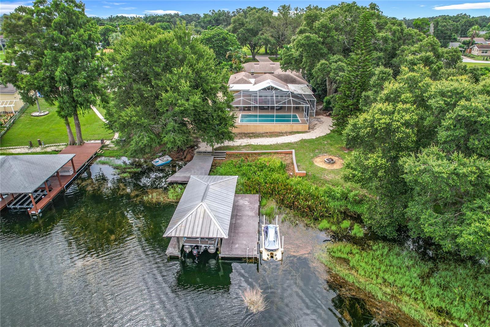 Welcome to 125 Lake Roy Drive—an extraordinary, move-in-ready lakefront estate delivering the true Florida lifestyle with zero compromises and no HOA. Set on a beautifully landscaped lot with ample parking for vehicles, boats, RVs, and lake toys, this home offers unmatched flexibility and convenience for waterfront living. Perfectly positioned on the prestigious South Chain of Lakes, this single-level pool home features panoramic water views, a private boat dock with lift, a brand-new jet ski dock, and nightly front-row seats to the LEGOLAND fireworks. With effortless access to more than a dozen interconnected lakes, this is a rare opportunity to own a true waterfront retreat designed for everyday luxury and unforgettable moments.
The home has undergone extensive upgrades, featuring a custom-designed kitchen with solid wood cabinetry, granite countertops, stainless steel appliances, a modern sink, and a new disposal. Both ensuite bathrooms were meticulously renovated, offering comfort and style in every detail. A brand-new HVAC system and ductwork have been installed, along with complete PEX re-piping, a new 1,000-gallon septic tank, and a five-chamber drain field, as well as a French drain across the entire driveway. Additional improvements include new flooring, fresh interior paint, upgraded trim, a new boat lift motor and cradle built for a pontoon, and a refreshed pool system for low-maintenance enjoyment.
Inside, the layout offers elegance and flexibility. The primary suite is tucked away for privacy and relaxation, while the second guest suite features an en suite bathroom that opens directly to the pool—perfect for extended family, guests, or a future in-law suite setup. A wood-burning fireplace anchors the spacious living area and opens to the lanai through six sets of glass doors, creating a seamless connection to the outdoors. A light-filled sunroom offers peaceful views of the pool and lake year-round, while a private, palm-lined courtyard provides a tranquil space for morning coffee or evening reflection.
The property also features two garages with space for three vehicles, as well as a dedicated carport. Conveniently located near major retail, dining, and downtown Winter Haven, this home offers a unique blend of privacy, convenience, and a true waterfront lifestyle. This property is also located near the Polk Parkway and Highway 27, giving you quick access to I-4, major metro areas, world-class theme parks, and local beaches in every direction.
Evening showings are highly recommended to fully experience the brilliance of the sunset over Lake Roy, best enjoyed from the tranquil comfort of this poolside sanctuary.