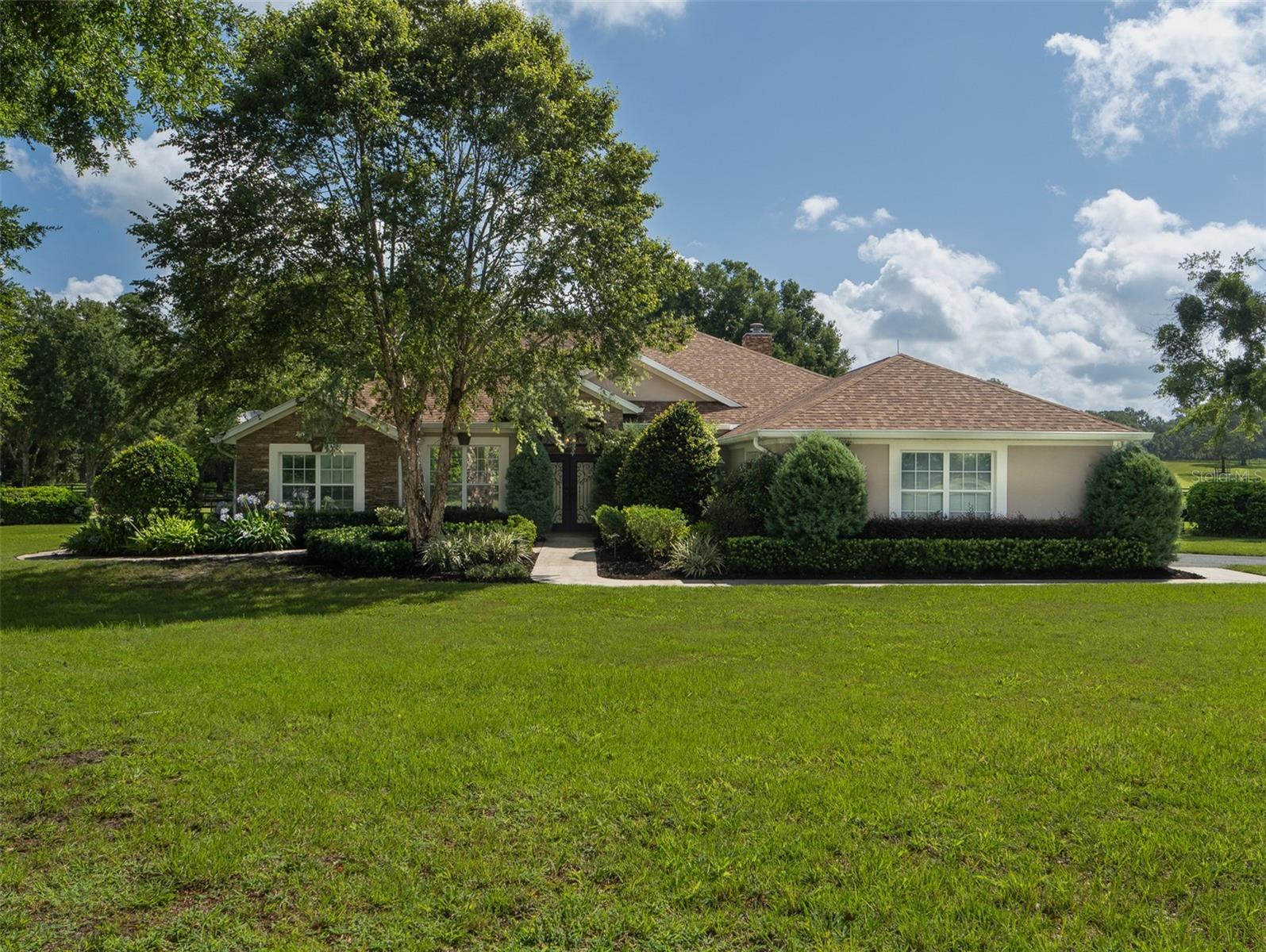 Welcome to this exceptional 13-acre equestrian estate located in the heart of Ocala, Florida. Fully fenced and offering complete privacy, this property is ideally situated less than five minutes from the World Equestrian Center and just 12 minutes from HITS! Designed for both equestrian functionality and comfortable living, the property features a well-appointed 5-stall barn with a wash rack, tack room, feed room, and office. An arena with GGT footing and four beautifully maintained paddocks provide excellent space for training and turnout. A spacious 4-bay garage/workshop with roll-up doors offers ample storage and workspace. The home offers a split floor plan with four bedrooms, three bathrooms, and a dedicated office. High ceilings and large windows fill the home with natural light, while the flooring combines tile, wood, and carpet in the bedrooms for a balance of style and comfort. The master suite has its own fireplace and a spa-like bathroom featuring a large tub surrounded by glass block windows, decorative pillars, chandeliers, dual vanities, a walk-in shower, and a generous walk-in closet. The kitchen is thoughtfully designed with a center island, abundant counter and cabinet space, a wine cooler, and a prep/bar sink—perfect for both everyday living and entertaining. Sliding glass doors from the living area open to a screened-in, in-ground pool, creating a seamless indoor-outdoor lifestyle. The property also includes a picturesque pond with a fountain, enhancing the peaceful, park-like setting. Offering a rare combination of privacy, convenience, and equestrian excellence, this property is a true gem in Florida’s horse country.
