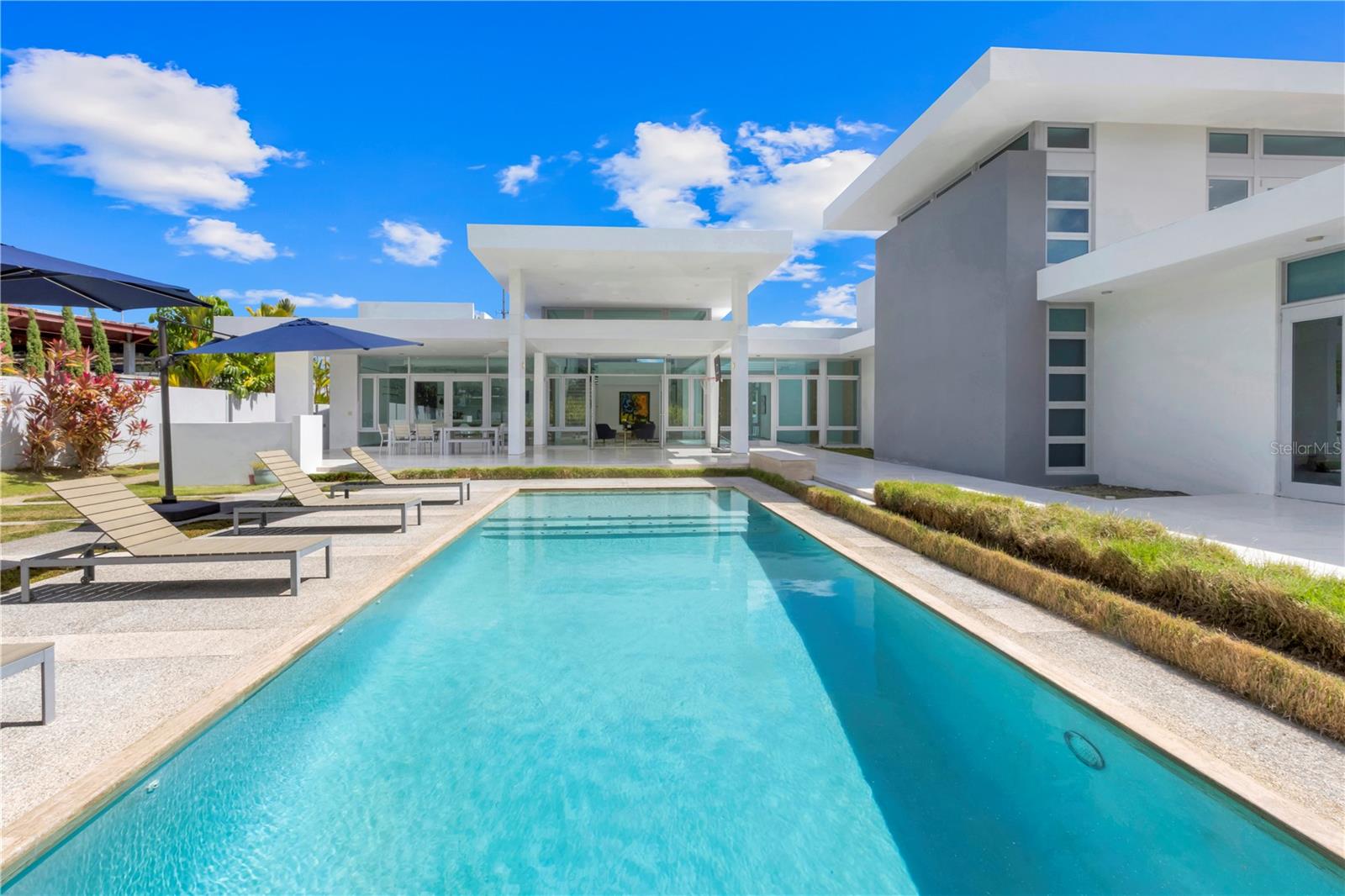 Nestled in the heart of the Santa Maria gated community in San Juan, this 7,494-square foot estate is set on an expansive and completely level lot on Mimosa Street, offering the perfect balance of modern luxury and island comfort. Boasting high-end finishes throughout, this meticulously designed property features custom millwork, a state-of-the-art Lutron system, and top-of-the-line kitchen appliances, ensuring a lifestyle of elegance and convenience. Whether hosting grand gatherings or enjoying intimate moments, the open and expansive floor plan with its high ceilings and ample natural light provides space for both relaxation and entertainment.
Step outside to your private oasis— complete with pool and covered terrace —ideal for enjoying the island’s beautiful climate year-round. In addition, the home is equipped with 100 solar panels, ensuring energy efficiency and sustainability, while a back-up power system and water cistern provide peace of mind in every season. Make this magnificent estate your next home and experience unparalleled luxury in one of Puerto Rico's most sought-after locations.
