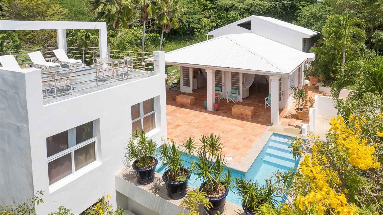 La SerenÃsima is a rare and timeless property located on a private cul-de-sac in the desirable Bravos de Boston neighborhood of Vieques. Designed with Caribbean sensibility and built in 1993 by the respected firm Cristofol, Hernández-Dupuy, this custom home sits on a lush, one-acre parcel of fully fenced land surrounded by mature gardens and tropical trees that provide exceptional privacy.
The property features two structures connected by an outdoor living area and L-shaped marmolite pool. The main residence includes a vaulted living room with exposed beams and terracotta Saltillo tile floors that continue throughout the home and patio areas. French doors open to the pool terrace, capturing trade winds and maximizing cross-ventilation.
Upstairs are two spacious bedrooms, each with air conditioning and a dedicated bathroom. The primary suite includes both an interior bath and a private outdoor courtyard shower. The open-concept kitchen features soaring 21-foot ceilings, built-in shelving, and generous counter space, offering both elegance and function.
The second structure is a self-contained studio with a kitchen, bathroom, and private rooftop sundeck accessed by a spiral staircase. Below the studio is an enclosed flex space ideal for storage, a workshop, or future creative use.
The pool area, surrounded by natural landscaping, is designed for relaxing or entertaining. At 4 feet deep and 5 feet wide with built-in steps, it offers a refreshing spot to cool off under the Caribbean sun.
The acre of land is sloped and usable, offering a rare combination of privacy and possibility. There is ample room for expansion—whether through the addition of guest casitas, recreational amenities, or further gardens—yet the existing mature landscaping already creates a natural buffer from neighboring properties and street noise.
Every room in the home is designed to interact with the outdoor environment, emphasizing indoor-outdoor living. The home has never been used as a rental and has been meticulously cared for by its original owners.
With three bedrooms, three bathrooms, two kitchens, multiple living areas, and outdoor amenities including a pool, patios, and rooftop deck, this property offers both comfort and flexibility. It is well suited as a primary residence, seasonal home, or multigenerational retreat.
Located centrally on the island, this Bravos de Boston property offers easy access to both beaches and town amenities while feeling like a secluded retreat.
This is a thoughtfully designed and well-constructed home that balances craftsmanship, natural beauty, and modern convenience—an exceptional opportunity on the island of Vieques.