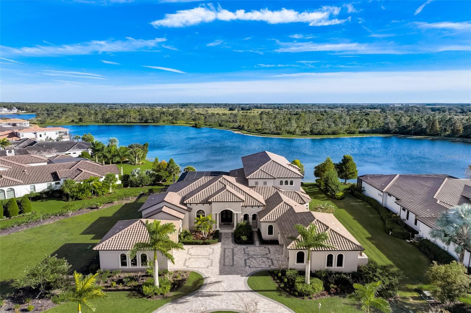 The Concession has been ranked as one of the TOP 10 Golf courses in Florida. When rivals collaborate, boundaries are broken and something special happens. The Concession Golf Club in Eastern Manatee County is the culmination of years of planning and design by Jack Nicklaus and Tony Jacklin, resulting in the ultimate tournament level course, surrounded by exquisite natural beauty. The estate homes in The Concession are an extension of that drive for excellence. Beyond the norm of luxury and with no homes surrounding the courses for ultimate privacy, homes throughout the community are examples of masterful design and uncompromising craftsmanship. 8407 Broadstone Court is a sprawling Mediterranean estate, situated on a picturesque 1.5 acre lot with long lake views to the Southeast, for the morning sun to welcome each day. The home encompasses 10,213 square feet, with 6,816 square feet under air, offering 5 spacious bedrooms and 6.5 luxurious baths. Richly finished with the finest of materials and attention to detail, the arched, wrought iron front door opens to soaring ceilings, open spaces with clean site lines and architectural details befitting a luxury estate. The kitchen is a dream for entertaining and enjoys open design for effortless flow to conversation spaces for lively parties or quiet evenings with family and friends. Expansive gleaming quartz surfaces perfectly complement the rich wood tones of the espresso cabinetry and stainless appliances, including a 6-burner gas cooktop with griddle, steam oven, hidden walk-in pantry, and Sub Zero Refrigerator and Sub Zero Freezer. Picturesque views of the tranquil lake are a feature throughout this home, and those views are on full display through panoramic screens that frame the lanai. The heated, salt water pool and spa are a classic Roman design and are accented by a built-in fire table for cool evenings and a 2 spacious lanais with access to the well-equipped Summer kitchen from one, and to the Primary Suite from the other. The primary suite is a palatial retreat, with a light-filled sitting room and a luxurious spa bath. 2 additional bedrooms(1 en-suite) are found on the first floor, with a well-appointed office and a bonus room downstairs as well. Upstairs are 2 more spacious guest rooms, a 2nd bonus room, and a perfectly positioned balcony to enjoy those sunrises over the lake. The home includes garage spaces for 4 cars, 2 EV charging stations, and enjoys a long pavered drive with a circular approach to graciously host parties and events. Need additional garage space? Build your dream garage or a guest casita! The Concession is a very special gated community, bistro restaurant onsite, along with a premium on privacy, luxury, and an elevated lifestyle, while enjoying close proximity to all of the amenities of the area, including award winning Lakewood Ranch, Sarasota and the diverse arts community, and Bradenton’s beautiful beaches. Unbelievably, this home has only been occupied 3 months in total. Wonderful chance to basically purchase new construction on acreage. Please click on the 2nd Virtual tour for an interactive floor plan experience and new pictures.