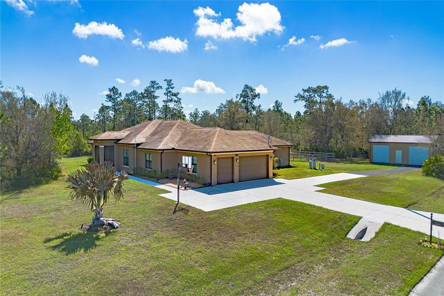 Set on 2.33 acres across two parcels, this single-story residence offers space, privacy and flexible living with no homeowner's association restrictions. The property includes a 1.3-acre homesite and an adjacent 1.03-acre vacant lot, creating room for recreation, gardening or future possibilities. Fenced areas provide space for pets, and a raised garden bed supports vegetables, herbs or flowers.
Designed with open sightlines and entertaining in mind, the home features 10-foot ceilings, tray ceilings reaching approximately 12 feet and 8-foot interior doors throughout. The expansive 31-by-31-foot great room is anchored by a tray ceiling and a 16-foot-wide floor-to-ceiling disappearing sliding glass wall that connects interior living areas to the outdoor entertaining spaces. Twelve ceiling fans and large openings allow natural light and airflow throughout the home.
The 24-by-15-foot kitchen centers around a large island with stainless steel sink and ample preparation space, positioned to serve both everyday living and gatherings. Additional entertainment spaces include a 24-by-19-foot game room with tray ceiling and a dedicated 12-by-19-foot theater room featuring a 7-inch raised rear platform and four theater-style seats.
The private primary suite measures approximately 19 by 19 feet and includes a tray ceiling and walk-in closet. Three additional bedrooms measuring approximately 12 by 15 feet, 15 by 14 feet with walk-in closet and 16 by 12 feet offer flexibility for guests or household members. A 16-by-14-foot office provides a dedicated workspace.
Outdoor living begins with a 40-by-16-foot covered and screened lanai featuring an outdoor kitchen with sink, granite countertop and grill hood. Two additional 30-by-6-foot screened lanais extend the living areas. The open-air pool includes two beach-entry shelves with bubbler features, four spa jets and two deck jets.
Additional features include two tankless water heaters, dual-zone heating and air conditioning systems, a three-car garage and RV parking. A 36-by-24-foot steel building with two 10-foot overhead doors and a walk-in door provides space for storage, workshop use or hobby equipment.
This property combines acreage, indoor and outdoor entertaining areas and versatile outbuildings in a setting designed for privacy and flexibility.