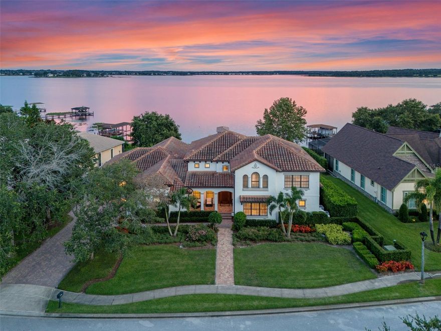 Extraordinary lakefront estate, where culinary excellence meets waterfront paradise. Immerse yourself in the ultimate lakefront lifestyle at this breathtaking direct waterfront estate on Johns Lake, where every morning begins with sunrise reflections dancing across 2,500 acres of pristine water and every evening concludes with golden sunsets painting the sky from your private south-facing sanctuary. This magnificent 4,800=-square-foot home in a gated community represents the pinnacle of Florida waterfront living, blending indoor luxury with endless aquatic adventures right outside your door. This amazing gourmet kitchen showcases stunning one-piece stone countertop that flows seamlessly across the expansive workspace in a single level, creating visual drama and the kitchen's design brilliance extends to its abundance of new custom cabinetry, meticulously crafted to maximize storage and style, with a cleverly hidden walk-in pantry. A charming breakfast nook features built-in bench seating positioned to capture the lake view. The built-in bar area elevates entertaining with its ice maker, wine refrigerator and elegant bottle storage/display options, allowing hosts to craft cocktails. A formal dining room is spacious enough to comfortably accommodate 10 guests beneath a gorgeous statement light fixture. Your waterfront lifestyle extends far beyond the home's solid concrete walls to encompass the entirety of Johns Lake where there are weekly fishing tournaments, peaceful kayaking or paddleboarding, water skiing and wakeboarding and leisurely pontoon cruises. Your new private dock, complete with boat lift, provides immediate access. This five-bedroom, three full and two half-bath residence offers dual primary suite luxury with one retreat on each level. The main floor primary suite captures gorgeous lake views through expansive windows, features a romantic corner fireplace elegantly set in travertine and has a generously sized walk-in closet with custom organizers. The bath presents a freestanding soaking tub, a beautiful glass-enclosed shower, dual vanities and a built-in makeup desk. The fifth bedroom on the main level provides flexibility as either guest accommodation or home office. The elegant spiral staircase, adorned with wrought iron and wood railings is dramatically illuminated by an amazing multi-level drop pendant light fixture. Here, an incredible theater room with comfortable seating transforms movie nights while the huge upstairs family room offers space for a second family room. The second primary suite offers those same lake views, has a large walk-in closet and gorgeous bath. Additional guest bedrooms, including a rear bedroom that captures amazing vistas, ensure comfortable accommodation for family and visitors. Large laundry room with custom cabinetry and utility sink, garage entry area includes built-in seating and storage solutions for shoes, backpacks and everyday essentials. The three-car garage, crown molding and new flooring throughout the home create a cohesive atmosphere of refined elegance. Fantastic location as the Florida Turnpike is three minutes away, dramatically reducing commute times. This remarkable lakefront estate represents more than a home. It embodies a lifestyle where gourmet culinary experiences unfold against a backdrop of endless water views, where morning coffee transitions seamlessly into afternoon water sports and where every sunset provides daily reminder of life's extraordinary possibilities.