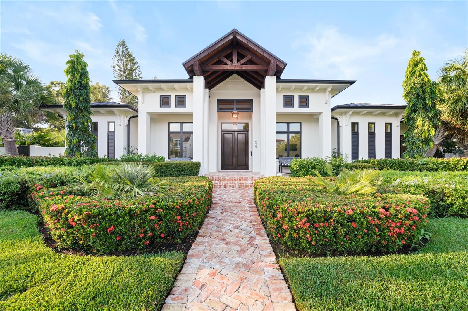 Located on a rare double lot within Flood Zone X, this 2021 custom-built residence blends timeless craftsmanship with modern comfort. From the herringbone brick walkway to the tongue-and-groove front porch, the attention to detail is evident from the start. Solid block construction and a 50-year standing seam metal roof provide lasting durability, while professionally landscaped grounds, irrigation on a private well, hurricane-impact windows, foam insulation, a whole-home generator, and a state-of-the-art security system offer peace of mind.
Inside, soaring ceilings, abundant natural light, and French doors connect seamlessly to the resort-style backyard. A dedicated office with full closet and built-in mail drop adds convenience, while the gourmet kitchen boasts a Sub-Zero refrigerator, Viking double oven, Bertazzoni gas cooktop, quartzite counters, oversized island, built-in ice maker, and walk-in pantry. The open design links kitchen, dining, and living areas, anchored by a remote-controlled gas fireplace. An additional family room with beamed ceilings, antique glass accents, and a wet bar with ice maker and dual wine fridges creates an inviting gathering space.
Outdoor living shines with a heated pool, sun shelf, spillover spa, and a covered patio with tongue-and-groove ceiling, recessed lighting, dual fans, built-in grill, pizza oven, sink, storage, and dual trash receptacles. A poolside half bath and keypad alley entry with two extra parking spaces enhance privacy. The west-wing primary suite features dual custom walk-in closets and a spa-inspired bath with zero-entry glass shower, soaking tub, double vanity with built-in hampers, and private water closet. French doors open directly to the pool, blending indoor serenity with outdoor luxury. Two guest suites in the east wing include walk-in closets and designer baths—one with soaking tub, the other with walk-in shower.
The laundry room offers a farmhouse sink, marble backsplash, soft-close cabinetry, built-in desk, and secondary refrigerator. A two-car attached garage is paired with a climate-controlled single-car garage with mini-split A/C, epoxy floors, sink, and attic space—ideal for a gym, office, or studio. Additional highlights include seamless gutters, dual attic storage, surround sound (app-controlled), blackout shades, and a whole-house water filtration system. Powered by natural gas—including fireplace, chef’s range, pool heat, dryer, and pizza oven—this home is designed for both luxury and efficiency. A northeast side yard with generator and storage is perfect for pets or extra equipment. Just minutes from the dining, shopping, museums, and waterfront parks of Downtown St. Petersburg, this home offers a rare combination of elegance, durability, and Florida’s coveted indoor-outdoor lifestyle.