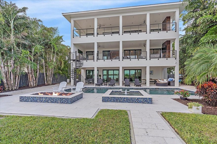 PRICE IMPROVEMENT!!! Experience the perfect fusion of coastal opulence and modern elegance within this waterfront residence located in one of Sarasota's most coveted zip codes: 34242, Siesta Key, home to the #1 beach in the USA. This turn-key oasis awaits your arrival. Built by the esteemed boutique firm, NC Ferguson Construction of Sarasota, this home exudes timeless charm and the functionality of new construction. Your backyard retreat where cherished memories will be made boasts 62 feet of waterfront AND a private beach, a rarity in itself to launch kayaks and paddle boards. Set sail from your own boat dock with jet ski lifts and a 10,000 lbs. boat lift, granting direct access to Little Sarasota Bay and the Gulf. Nestled amidst protected mangroves and meticulously landscaped surroundings, you'll discover an oasis of serenity and the lifestyle you've always dreamed of! This home offers a total of 8,256 sq. ft., including 5,034 sq. ft. of air-conditioned living space and 2,256 sq. ft. of covered balconies and patios. Enjoy the pool, spa, and gas-powered fire pit while relishing Little Sarasota Bay's unobstructed views. The residence features four bedrooms, three full bathrooms, and a separate home office on the second and third floors. On the spacious ground-level living space, you'll find an additional custom-built bunk-bed room, a luxurious aprés-swim full bathroom, and a piano/entertainment room that can also be utilized as a private gym. Begin your day with waterfront vistas and the soft glow of the sun reflecting off the bay, thanks to direct access to a covered balcony from your primary bedroom sanctuary. This exquisite suite encompasses a sitting area/library and features two impeccably designed walk-in closets, an en-suite bathroom with a soaking tub, dual vanities, and a glass-enclosed shower that offers breathtaking waterfront views from every angle while maintaining absolute privacy. The chef's kitchen, adorned with an expansive Quartz island, overlooks the dining and living areas, seamlessly integrating with a full wall of glass sliders that reveal awe-inspiring colors of the sunset and lush bay panoramas. Equipped with a six-burner Wolf stove and an array of Wolf appliances, including a coffee/espresso/cappuccino maker, this kitchen is a culinary masterpiece. Savor pristine water courtesy of the reverse osmosis water filtration system, which also connects to your luxury ice maker. Your Sub-Zero refrigerator and Asko dishwasher complete this epicurean haven. For grand gatherings, indulge in the football game on one of two patios with outdoor television monitors. As boats gracefully glide by, revel in your comprehensive outdoor kitchen, complemented by a custom exterior spiral staircase that leads to your waterfront patio sanctuary, offering another convenient access point to the ground level. This intelligent abode boasts full automation with remote access to landscape lighting and irrigation, boat lifts, a Sonos multi-zone indoor/outdoor speaker system, garage door controllers, a security camera system, interior lighting, pool/spa temperature and lighting controls, automated blinds, and wireless internet range extenders. The three-car garage ensures your vehicles are comfortably housed, and it even includes ports to easily install a Tesla charging station. This home welcomes you with open arms, fully finished and exquisitely adorned, ready for you to relish from day one. Paradise beckons – your home in paradise awaits…