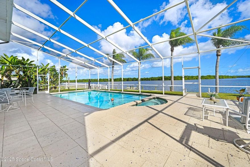 Endless water & nature vistas! Spacious home is perfectly positioned on premium navigable Sykes Creek frontage w/access to the Banana River, Indian River, Intracoastal Waterway, & ocean via nearby Port Canaveral Locks — a true boater's paradise. Oversized screened-in pool w/elegant paver deck is perfect for entertaining or relaxing. Huge family room offers warmth & charm w/wood-burning fireplace, wet bar, & sliders to patio. Updated eat-in kitchen w/beautiful countertops, convenient pass-through window to patio, & newer appliances. Meticulously maintained w/many recent updates: roof (2020), water heater (2022), Rain Soft water filtration (2018), screen enclosure (2018), dock (2019), new pool pump, Rhino Shield exterior coating, Massey termite bond, & two HVAC systems serviced annually. Classy vinyl fencing w/double gate for boat/trailer storage. Large bedrooms provide comfort & space, w/luxurious primary suite featuring his-&-hers closets, soaking tub, roomy shower, & dual sink vanity.
