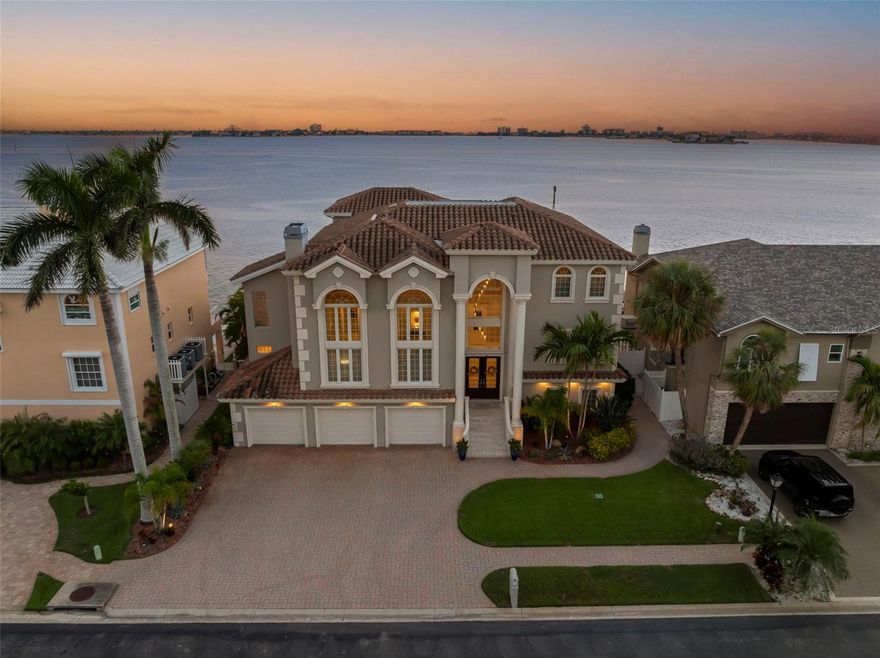 Welcome to an extraordinary waterfront residence in the highly sought after, gated Pasadena Yacht & Country Club. Perfectly positioned on the open waters of Boca Ciega Bay, this impeccably built all-block constructed estate combines timeless design with modern luxury, creating the ultimate Florida lifestyle retreat. A private elevator connects all levels of this home, which showcases soaring ceilings, elegant finishes, and expansive views from nearly every room. Double leaded glass doors open to a grand foyer and formal living room with cathedral ceilings, a stately gas fireplace, a wet bar for entertaining, and a striking glass-walled office. The main living level is designed for both intimate gatherings and grand entertaining. A formal waterfront dining room with marble flooring flows seamlessly into a chef’s kitchen with custom solid wood cabinetry, a center island, gas cooking, pantry, and breakfast bar overlooking the family room with a built-in saltwater aquarium and casual dining nook. Step outside to the spacious covered waterfront terrace, perfect for al fresco dining and enjoying spectacular sunsets. This level also features a state-of-the-art theatre room with elevated seating and a full bath. The top level is dedicated to private living spaces, with hardwood flooring throughout. The expansive primary suite is a true retreat, offering breathtaking water views, two walk-in closets, a private waterfront balcony, and a luxurious en-suite bath with dual vanities, a soaking tub, and walk-in shower. Three additional bedrooms, two with en-suite access and water views, provide comfort and space for family or guests. The ground level features a 3-car garage with additional garage door access to the waterfront, a large workshop, and ample storage for all your toys. Step outside to enjoy a brand-new resort-style outdoor living area, complete with a sparkling saline pool, a covered jacuzzi that flows into the pool, captivating water and fire features, and an expansive textured marble pool deck. Boaters will appreciate the new 50’x20’ composite dock with a 30,000 lb lift and a 10,000 lb lift, offering immediate access to Boca Ciega Bay and beyond. Additional upgrades include a newer Generac generator, new landscaping with outdoor lighting, crown molding, new hurricane rated picture windows in family room and primary suite as well new hurricane rated sliding doors on 1st floor.  Living here also provides the rare opportunity to bypass the waiting list and join Pasadena Yacht & Country Club within 30 days of purchase, unlocking world-class amenities right outside your door. This is more than a home—it’s a statement of luxury waterfront living.