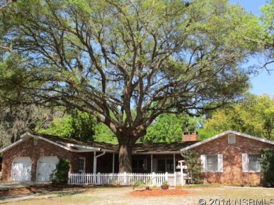 Nestled under the oaks this sprawling 4-5 bedroom home offers endless possibilities. Country living at it's finest just a short drive to upscale shopping, eateries, medical facilities, highways and to the beach! Situated on over 3+ acres this Old World brick home has many unique features including Pine Wood flooring, exposed brick accent walls, wood beams, fireplace, skylights and large open gathering areas. Kitchen has large center island with prep sink, tiled counters & beautiful brick hearth style cooking area featuring a Jennaire cooktop. Master bedroom has tiled flooring and updated bath & dressing area. Secondary bedrooms are ample in size with plenty of closet space. 4th bedroom has ensuite bath and would make a perfect inlaw/teen or extended family living area. 5th bedroom could easily be an in home office. Other inside features include security system, brick pavered foyer, & inside laundry. French doors lead to screened porch overlooking sparkling blue pool and patio area. Main home has a 2 car oversize attached garage. Exterior features a fabulous detached outbuilding w/soaring ceilings which can accommodate all the toys including an RV garage space, boat parking, or workshop. It is attached to a concrete block 4 stall barn with inside & outside stalls and tack room. Totally fenced pasture for horses. Back of property is adjacent to Spruce Creek. Looking for a multiple use property then put this one on your list.
