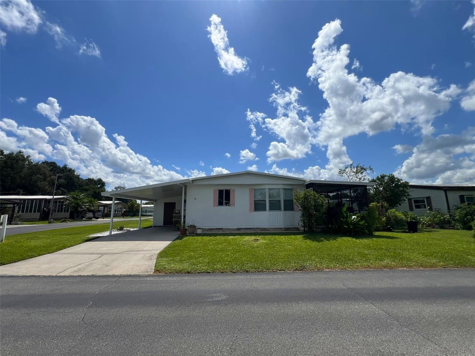 This spacious 2 Bedroom, 2 Bathroom manufactured home in the 55+ Floral Lakes Community in Bartow, Florida features double pane windows in the Primary Bedroom; a metal roof; a large Kitchen with new subflooring and finish flooring, along with newer cabinetry and a stylish oversize sink, ample storage & closet pantry; a Dinette area; a large Living Room with access to the rear screened porch. Primary Bedroom features walk in closet and en-suite bathroom with fiberglass shower. Guest bathroom features a fiberglass tub/shower combo. Luxury vinyl flooring in the common areas, carpet in the bedrooms. Full size washer and dryer (included) are located in the outdoor laundry room/workshop, under the single car carport.
Located in central Florida, between Tampa and Orlando, this golf cart friendly community is near the Bartow Civic Center, Bartow Public Library, and Mary Holland Park. Here you OWN YOUR LAND (no lot rent) and pay low monthly HOA fees. The Floral Lakes community offers access to a stocked pond with community boat ramp and dock. Clubhouse amenities include recreation space, shuffleboard, putting green, and large heated swimming pool. Social clubs, dances, exercise, pot lucks, and MORE! Association approval is required for purchase. Call your Realtor today for more information and to schedule a showing!