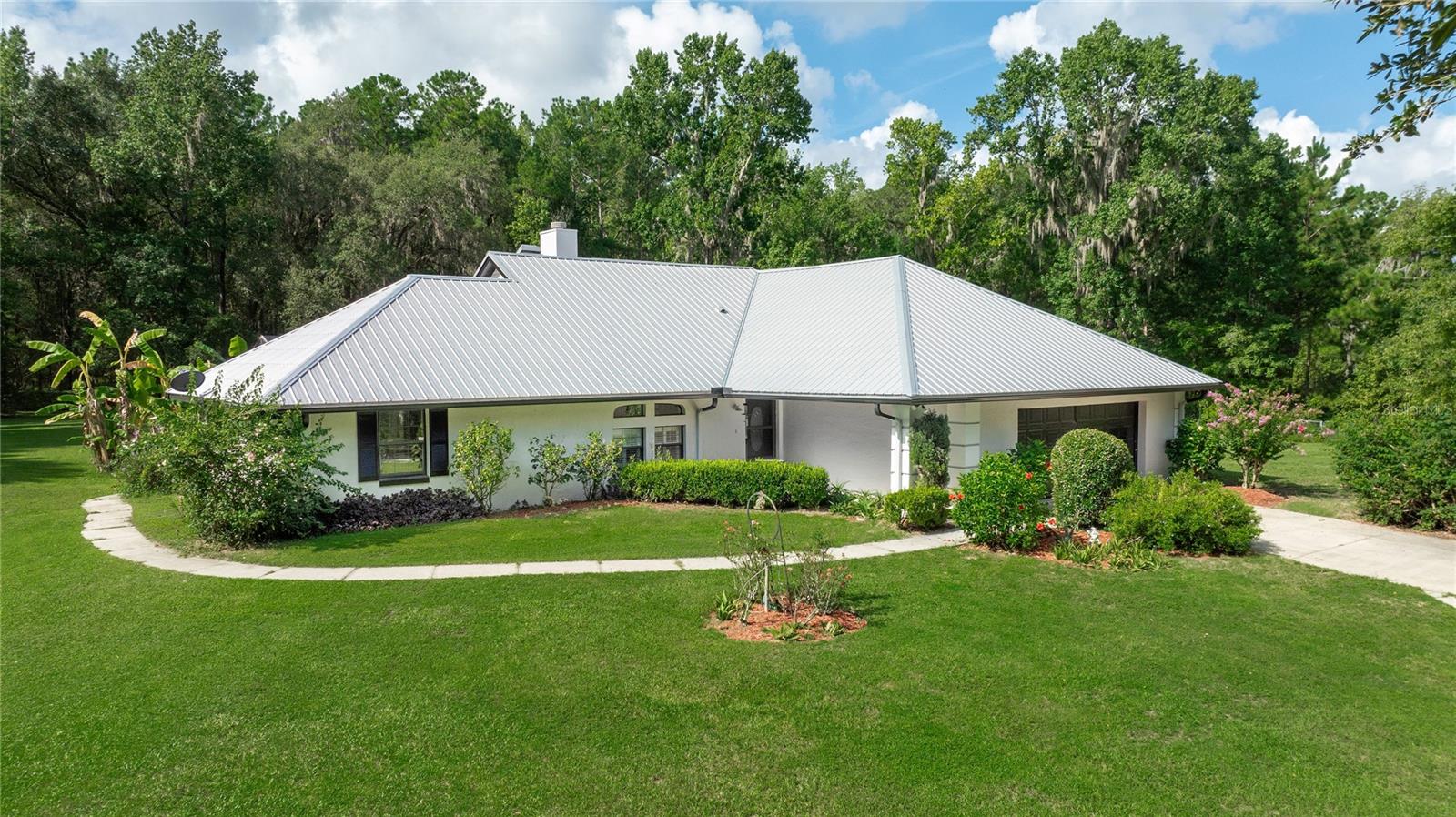 Nestled on 10 private, wooded acres just 5.5 miles from the World Equestrian Center, this 3-bedroom, 2-bath concrete block and stucco home offers the perfect blend of peaceful country living and everyday convenience. The open floor plan features vaulted ceilings, a cozy fireplace, spacious living and dining areas, and a well-appointed kitchen that flows into a bright enclosed sunroom—ideal for relaxing or entertaining. The split-bedroom layout includes a spacious primary suite with dual closets and an oversized ensuite bath, while the two guest bedrooms are generously sized with shared access to a second full bath. Outside, enjoy a screened in-ground pool, a 2-car garage, perimeter fencing, a durable metal roof, and two small fenced paddocks ready for your animals. Beautifully landscaped and thoughtfully designed, this property provides ample space, privacy, and a true sense of retreat—while still being just minutes from shopping, dining, Rainbow Springs, and top equestrian venues.