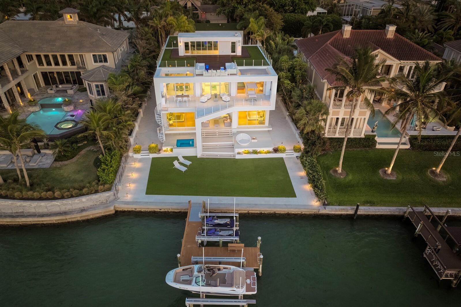 Modern marvel overlooking New Pass in Lido Shores! Step into this tropical escape through the hidden courtyard that connects the three-bedroom main home to the secluded, two-bedroom guest house with an expansive sundeck, 60-foot wet-edge lap pool lined with royal palms and unique fire bowls, as the perfect introduction to a contemporary masterpiece designed by DSDG Architect Mark Sultana and built by Voigt Brothers Construction. The exceptional concept behind this custom “picture frame” estate combines a sleek and innovative design with warm and comforting features, inspired by Sarasota’s School of Modern Architecture and the international modern architecture of Brazil. Boasting all the amenities required for luxury living, this SMART home’s inspired style highlights spectacular water views that stretch out to the Gulf of Mexico from just about every room of the nearly 6,600 square-foot interior, and you will instantly love the 360-degree vistas from the private rooftop terrace made of teak wood decking and putting green turf. Impressive features inside and out include maple wood, terrazzo, and porcelain tile (with a glass finish) flooring, gas fireplaces, custom built-ins, four-stop elevator, Lutron lighting system, gorgeous bathrooms with stone-top floating vanities, four new air-conditioners (2022), three gas tankless water heaters, and oversized four-car garage. As you enter the main residence through glass double doors, the suspended staircase with solid maple treads is backed by a modular art wall made of wavy plastered panels that create an impressive waterfall effect. Volume ceilings and walls of floor to ceiling impact glass sliders to the west and east ensure rooms are bright and airy. Guests can enjoy the first level, offering a gym, sauna, two bedroom suites with waterfront terrace access, studio with wet bar, and office. The reverse-style layout places the main living areas on the second level, optimizing the best of the views. The open concept of this level comprises the gourmet kitchen with its poured terrazzo waterfall edge island and Miele appliances, as well as the family room, living/dining room, and secluded master suite. Stacked glass sliders create a seamless transition to outdoor living, opening to the glass-railing terrace, summer kitchen, built-in grill, and spiral staircase that leads down to the waterside hot tub. Boaters will appreciate the deep-water dock with multiple lifts, newer seawall (2011), plus the direct, unobstructed access to the Gulf from New Pass. Walk to enjoy Lido Shores’ gated, private beach as a splendid finishing touch.